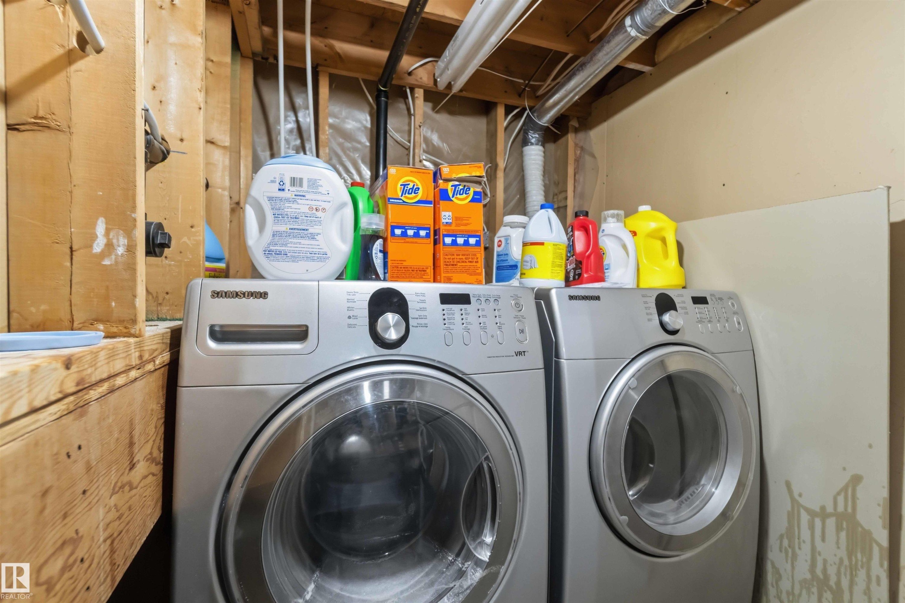 Dedicated laundry area featuring a side-by-side washer and dryer set, exposed wooden framing, and accessible overhead ductwork - 4428 11A Avenue Nw, Edmonton, AB - Indoor Photo Showing Laundry Room