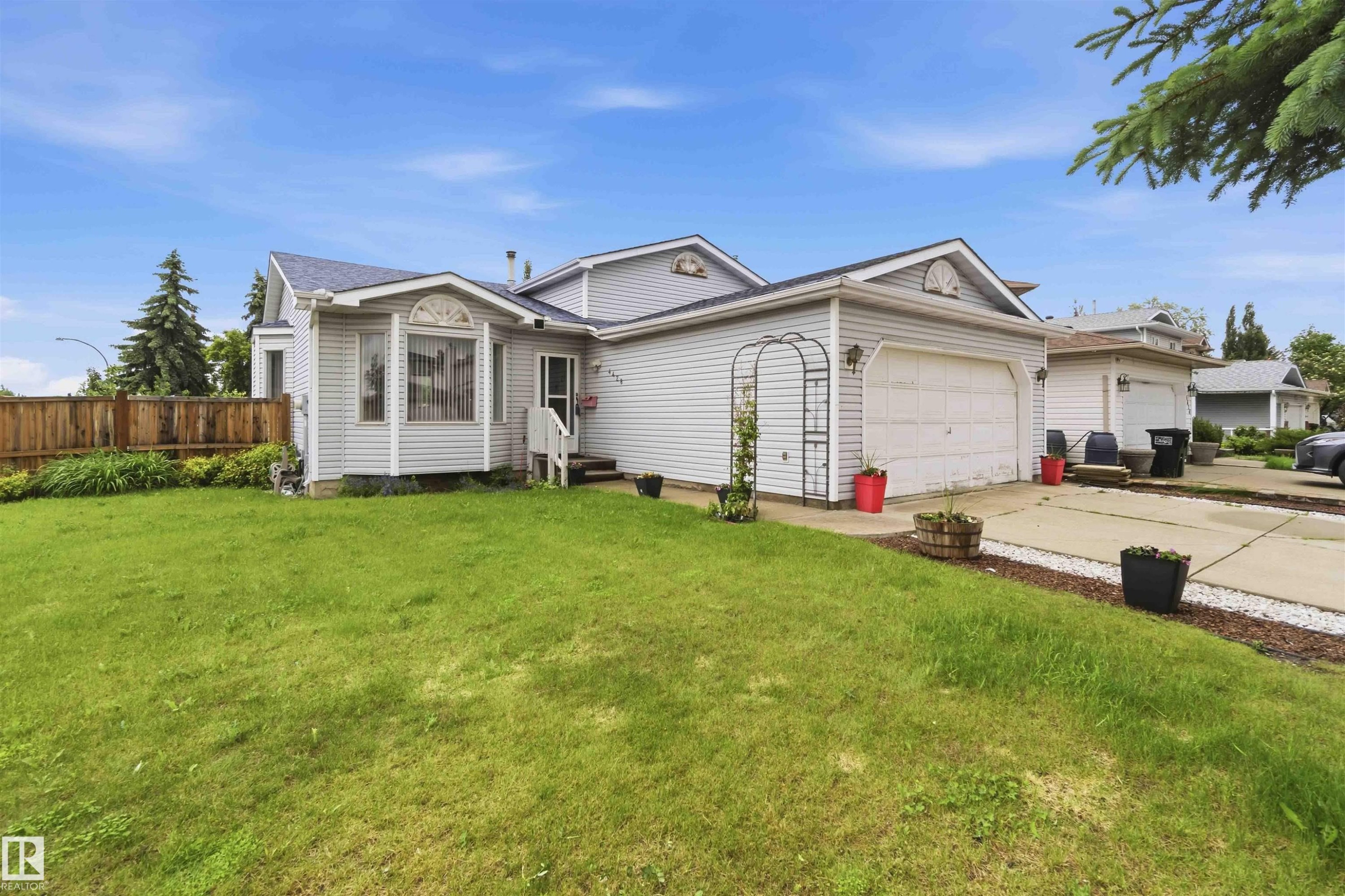 Property exterior featuring light-colored siding, an attached garage, a bay window, and a front lawn - 4428 11A Avenue Nw, Edmonton, AB - Outdoor