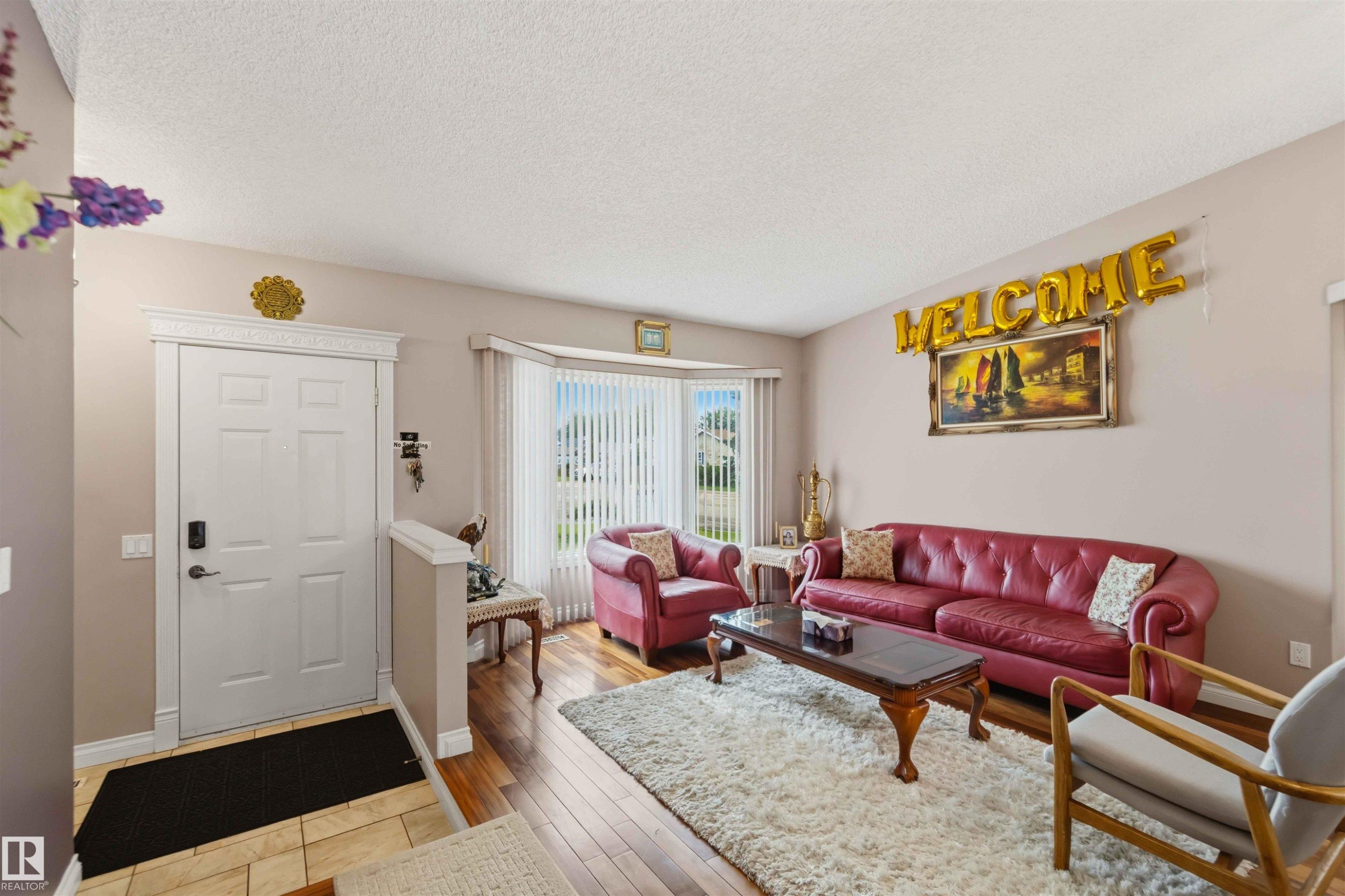 Formal living area featuring a bay window with vertical blinds, wood-finish flooring, and a decorative front entry door with ornate trim - 4428 11A Avenue Nw, Edmonton, AB - Indoor Photo Showing Living Room