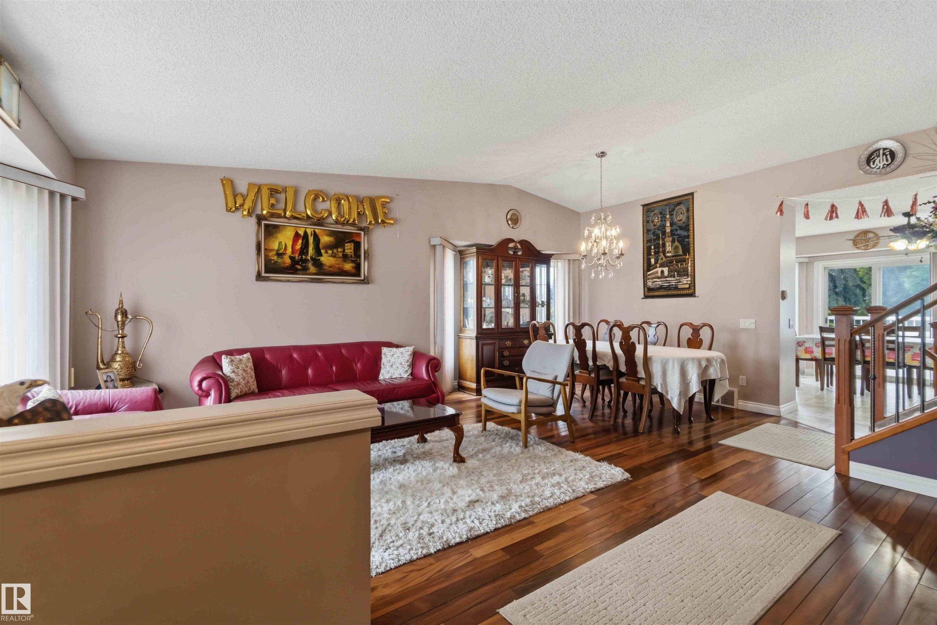 Open-concept living and dining areas featuring wood-finish flooring, a crystal chandelier, vaulted ceilings, and a staircase with wood railings - 4428 11A Avenue Nw, Edmonton, AB - Indoor Photo Showing Living Room