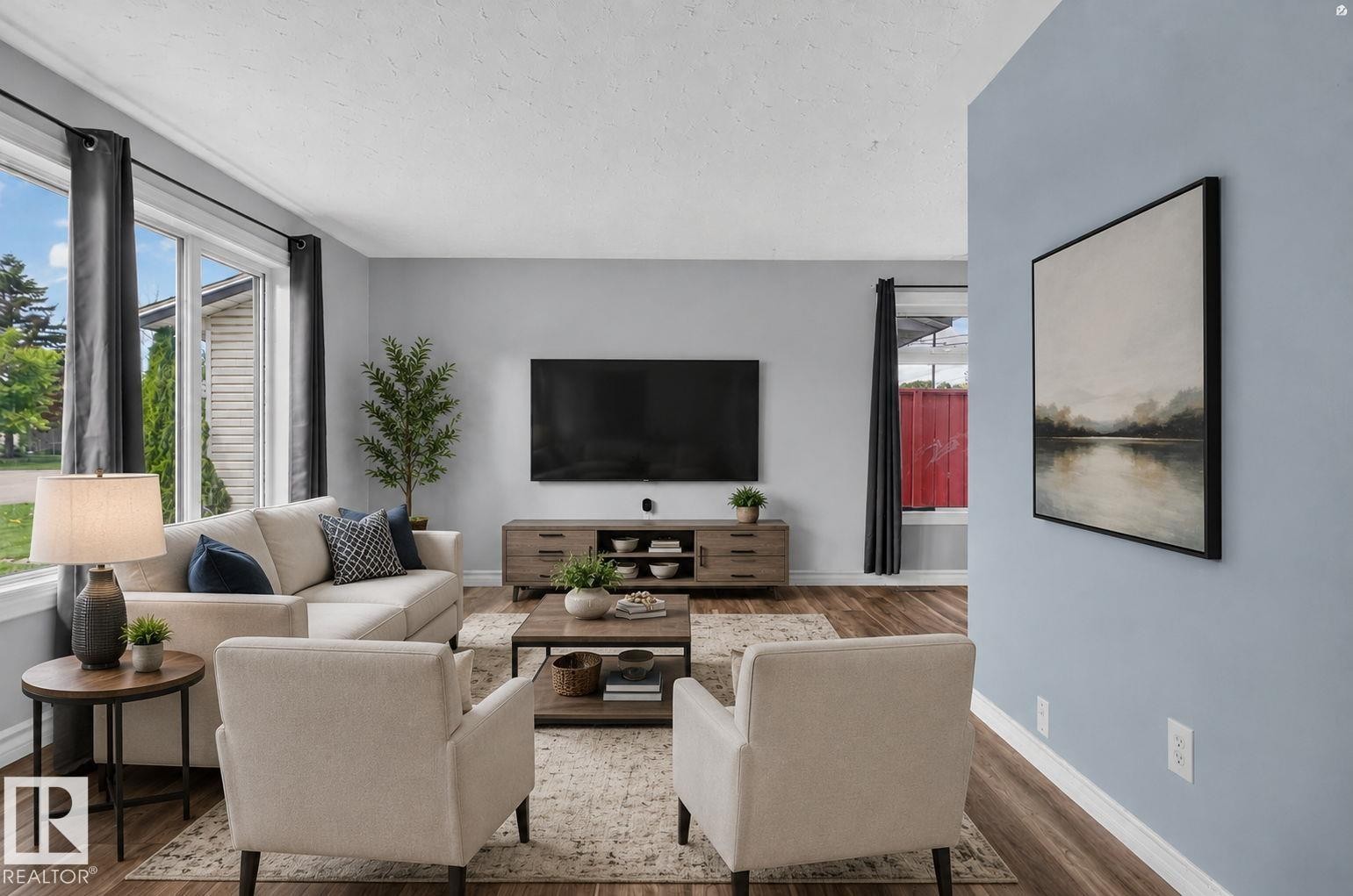 Spacious living area featuring large windows, wood-finish flooring, light blue wall paint, and white baseboards - 13431 109 Street, Edmonton, AB