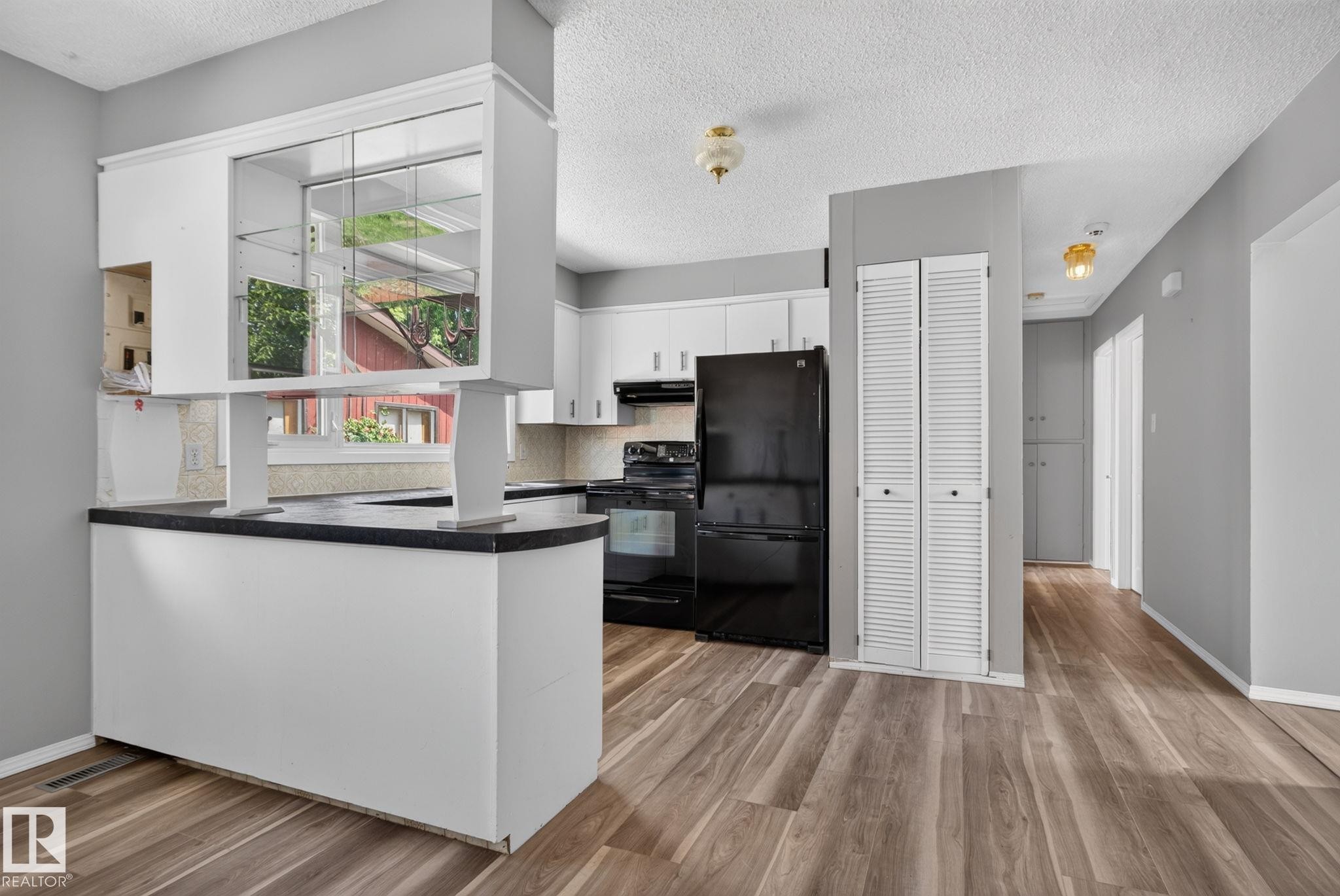Kitchen featuring white cabinetry, black appliances, dark countertops, wood-finish flooring, and a pass-through window with display shelving - 13431 109 Street, Edmonton, AB
