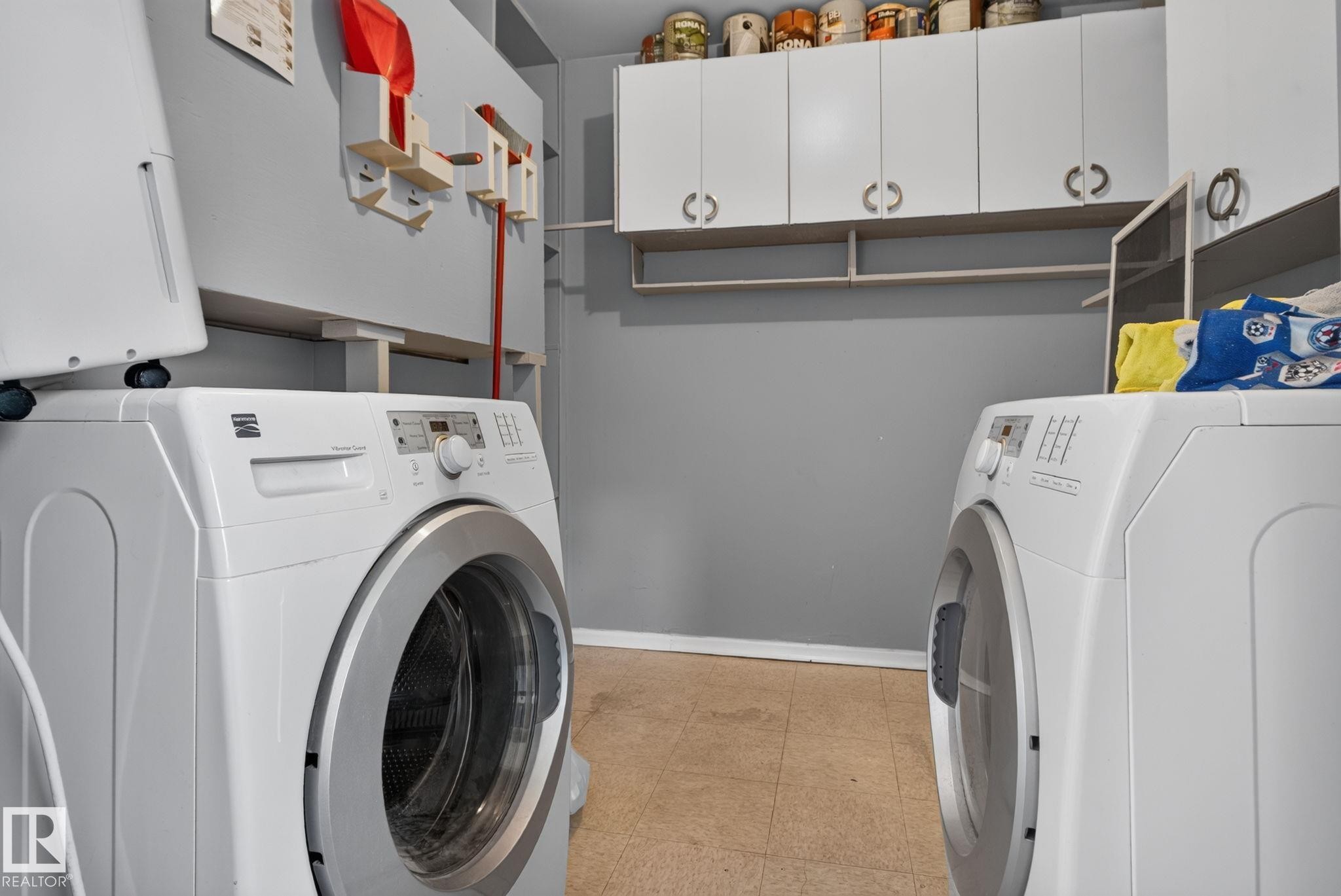 Dedicated laundry area featuring a front-load washing machine, built-in overhead cabinetry, open shelving, and neutral tone flooring - 13431 109 Street, Edmonton, AB