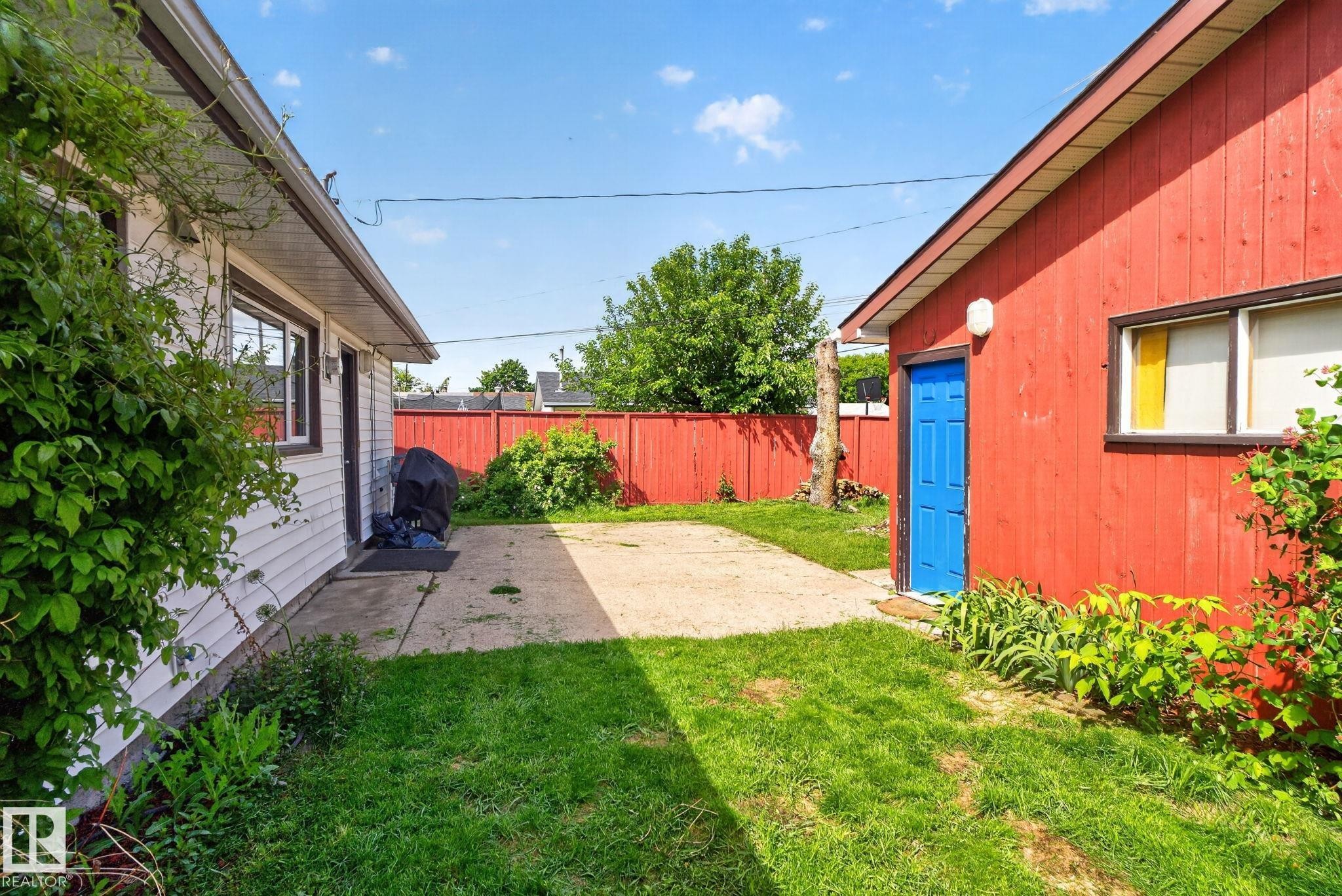 Spacious outdoor area featuring a concrete patio, green lawn, and a red privacy fence - 13431 109 Street, Edmonton, AB