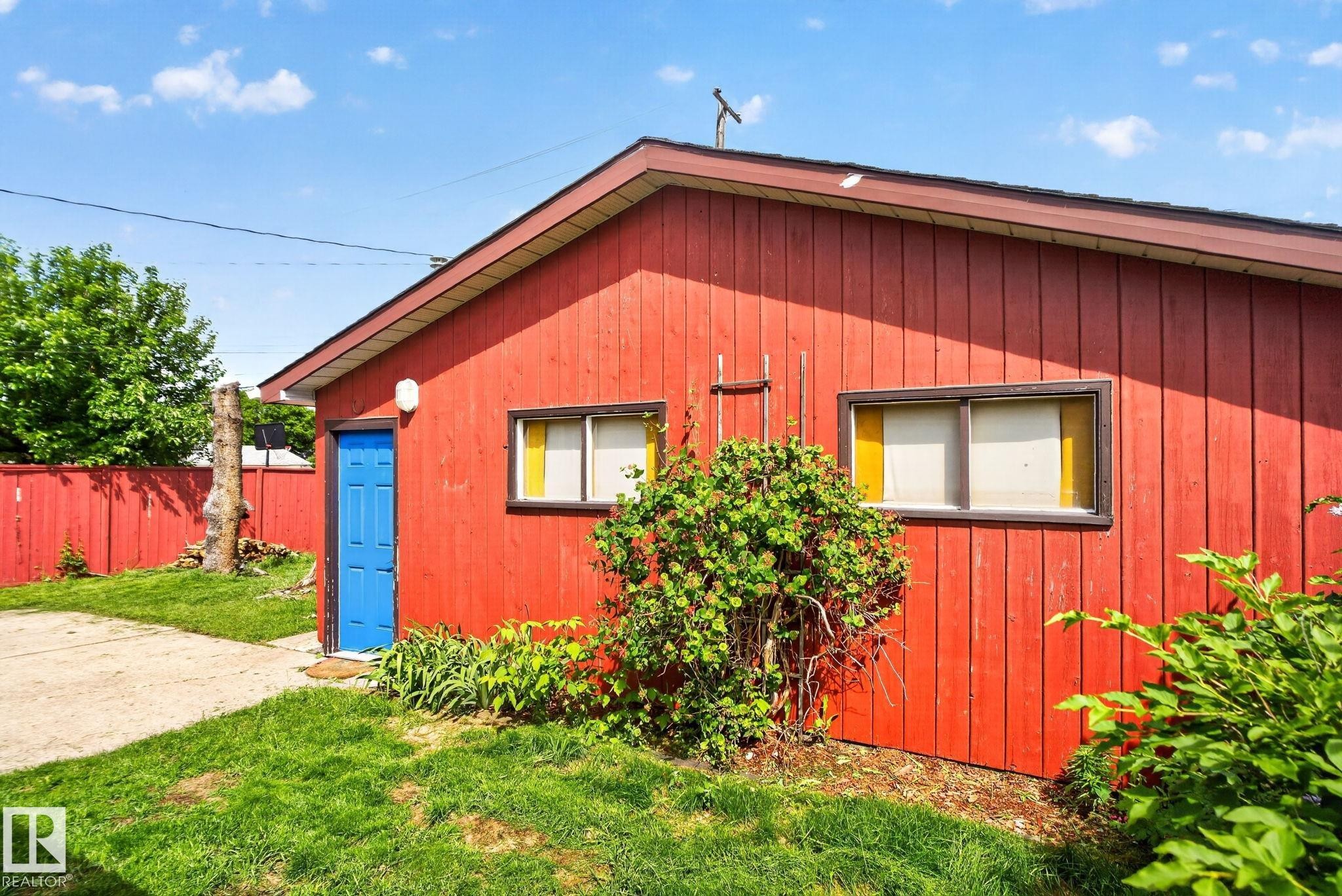 Red vertical siding exterior with a bright blue door, white trim, and a sloped roof - 13431 109 Street, Edmonton, AB