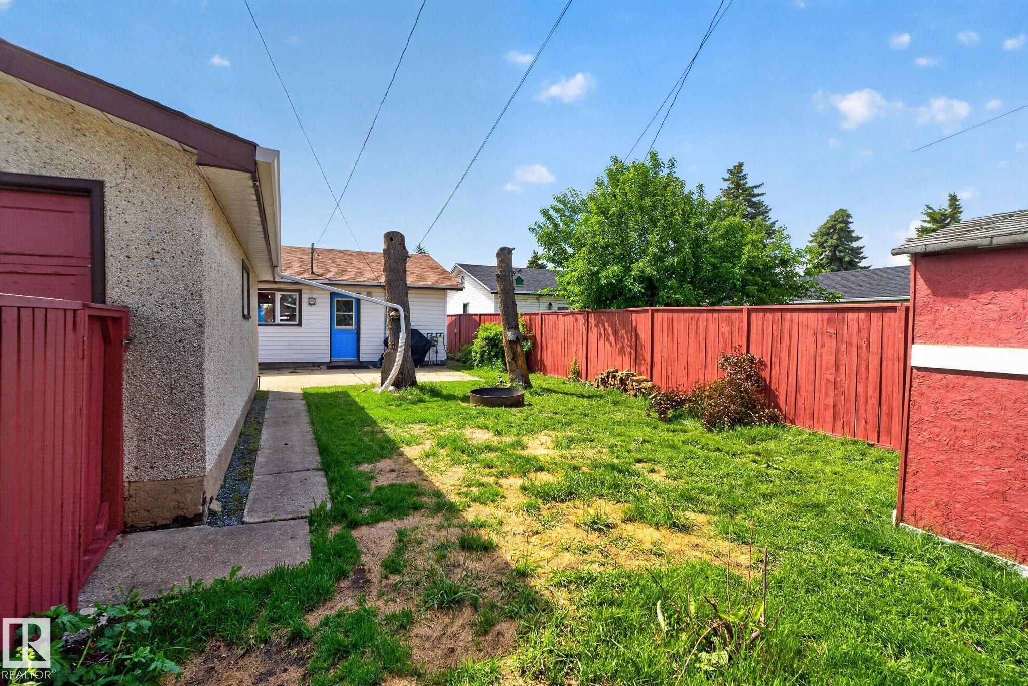 Expansive backyard featuring a vibrant red privacy fence, a concrete walkway, and a detached building with a blue entry door - 13431 109 Street, Edmonton, AB