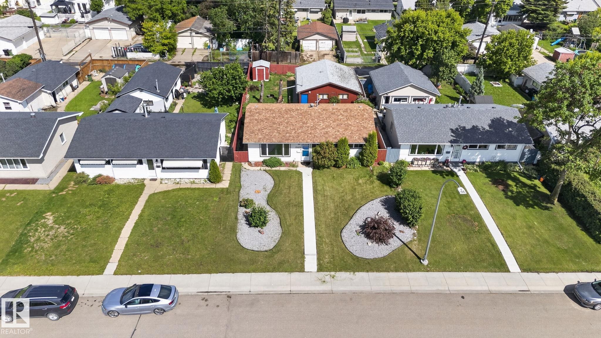 Property with a prominent front yard featuring a concrete walkway, two distinct landscaped rock gardens with plantings, and a mature tree - 13431 109 Street, Edmonton, AB