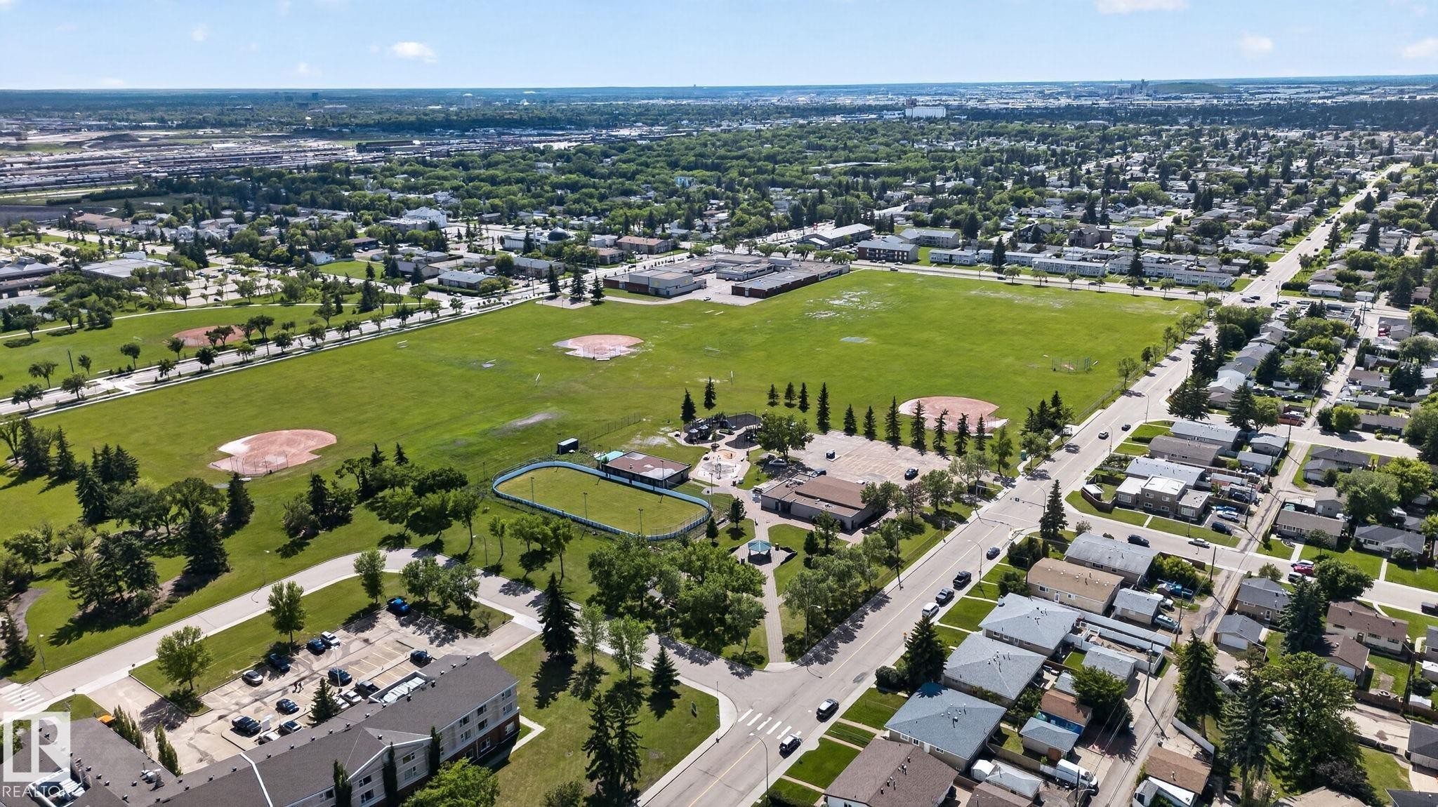 Expansive green space featuring multiple baseball diamonds, a track, and mature trees, surrounded by residential streets and urban landscaping - 13431 109 Street, Edmonton, AB