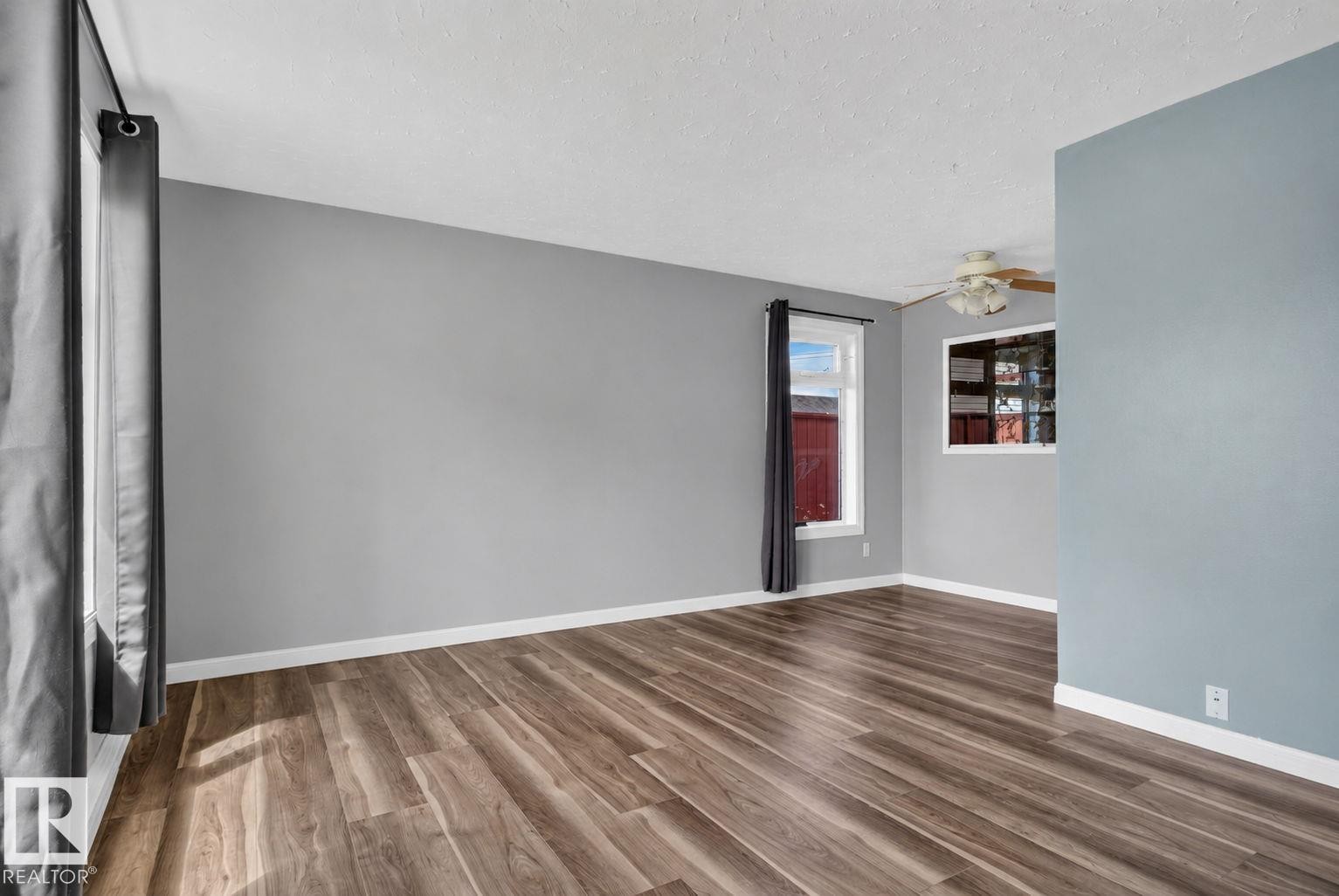 Spacious room featuring wood-finish flooring, light gray walls, white trim, and multiple windows providing natural illumination - 13431 109 Street, Edmonton, AB