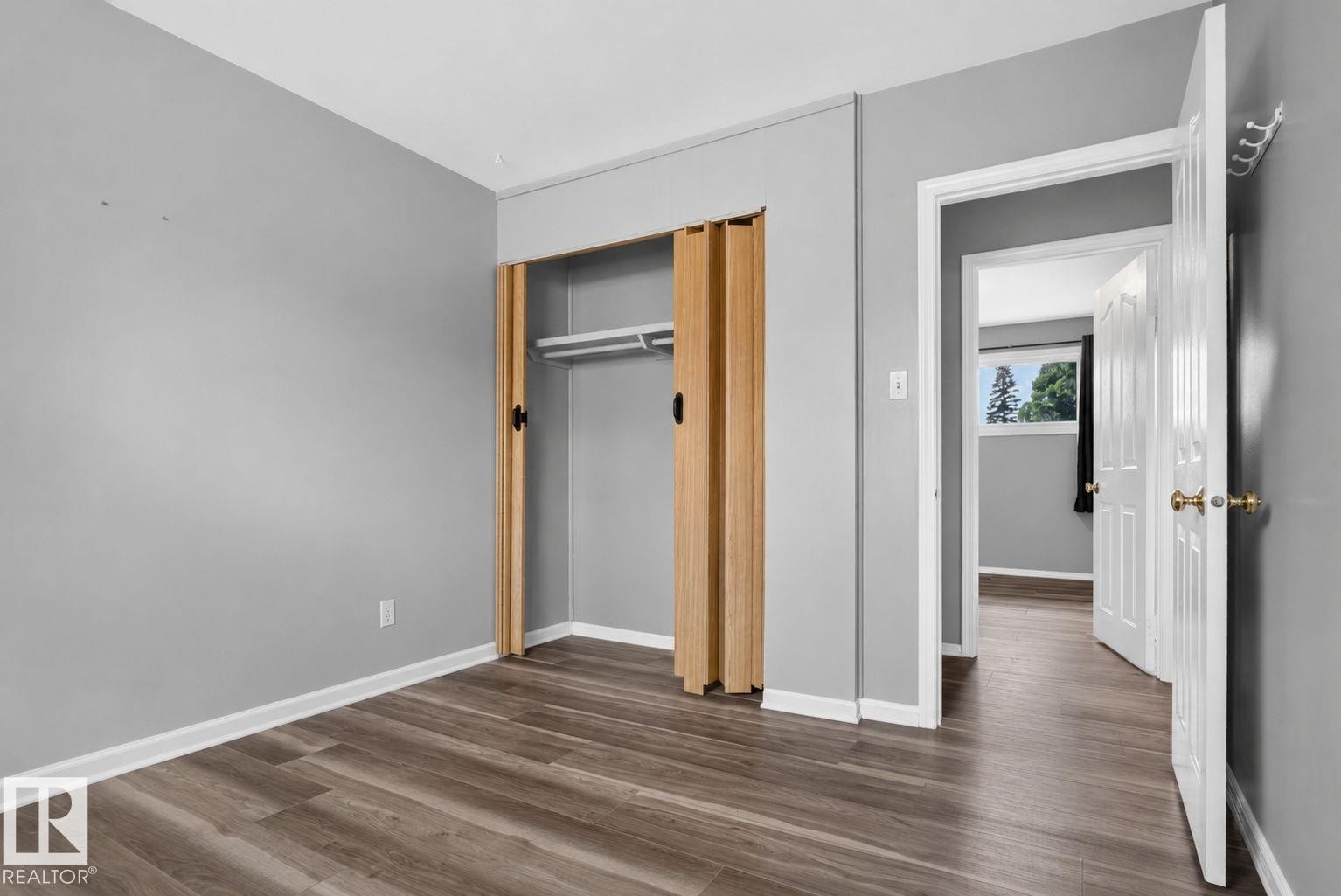 Interior room featuring wood-finish flooring, light gray walls, white baseboards, and a built-in closet with bi-fold doors - 13431 109 Street, Edmonton, AB