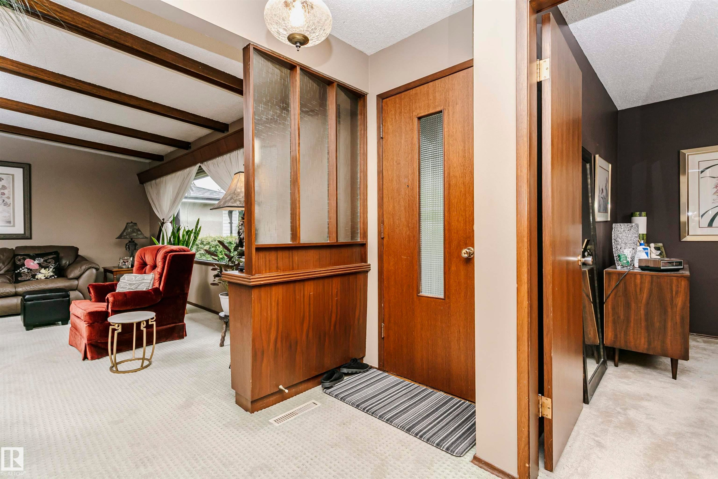 Entryway featuring a wood-finish door with frosted glass insert, an overhead decorative light fixture, and a partial wood-finish room divider with frosted glass panels - 14231 80 Street, Edmonton, AB