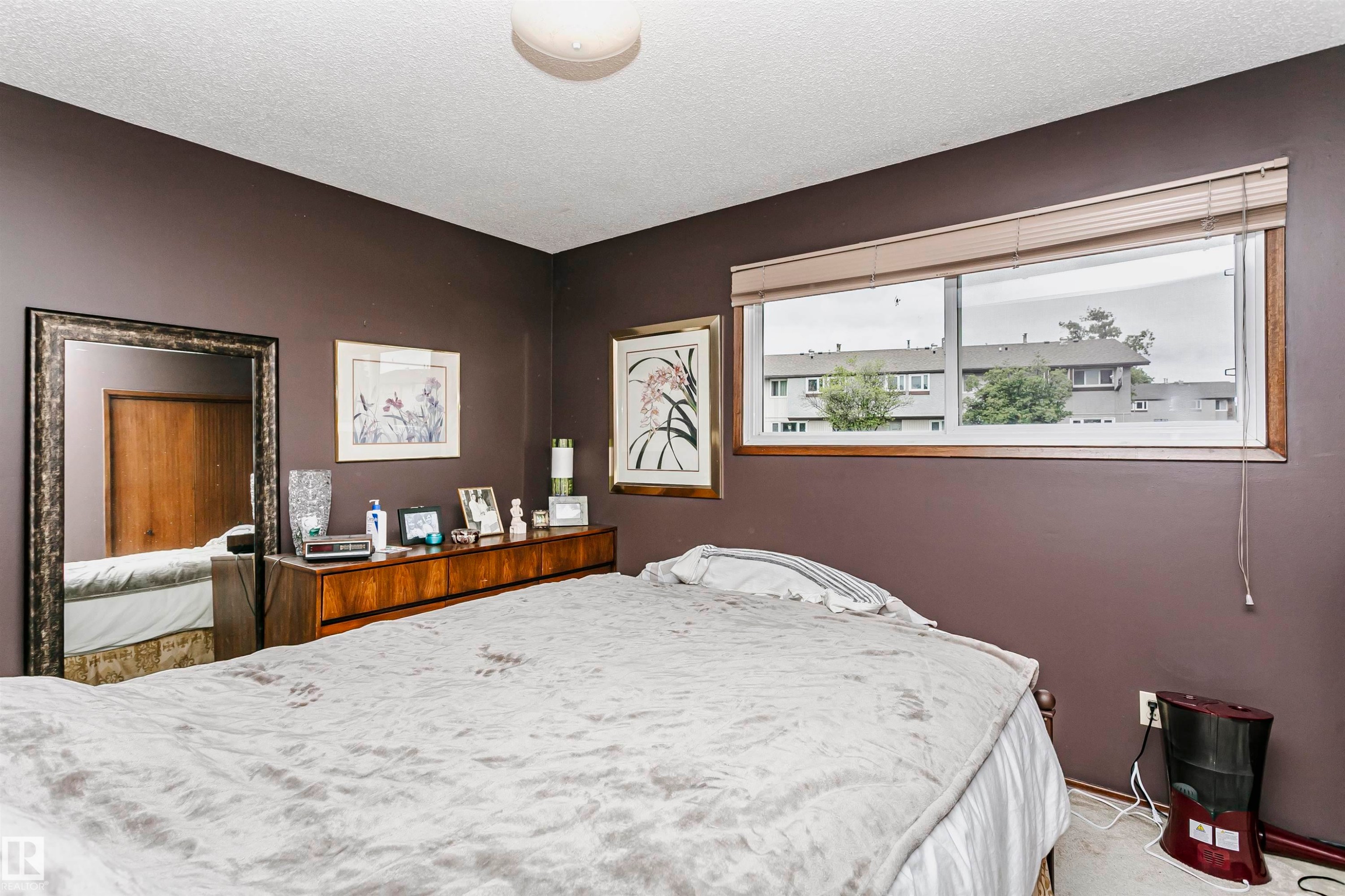 Room featuring a wide window with blinds, wood-finish window trim, a ceiling-mounted light fixture, and a built-in closet with a wood-finish door - 14231 80 Street, Edmonton, AB