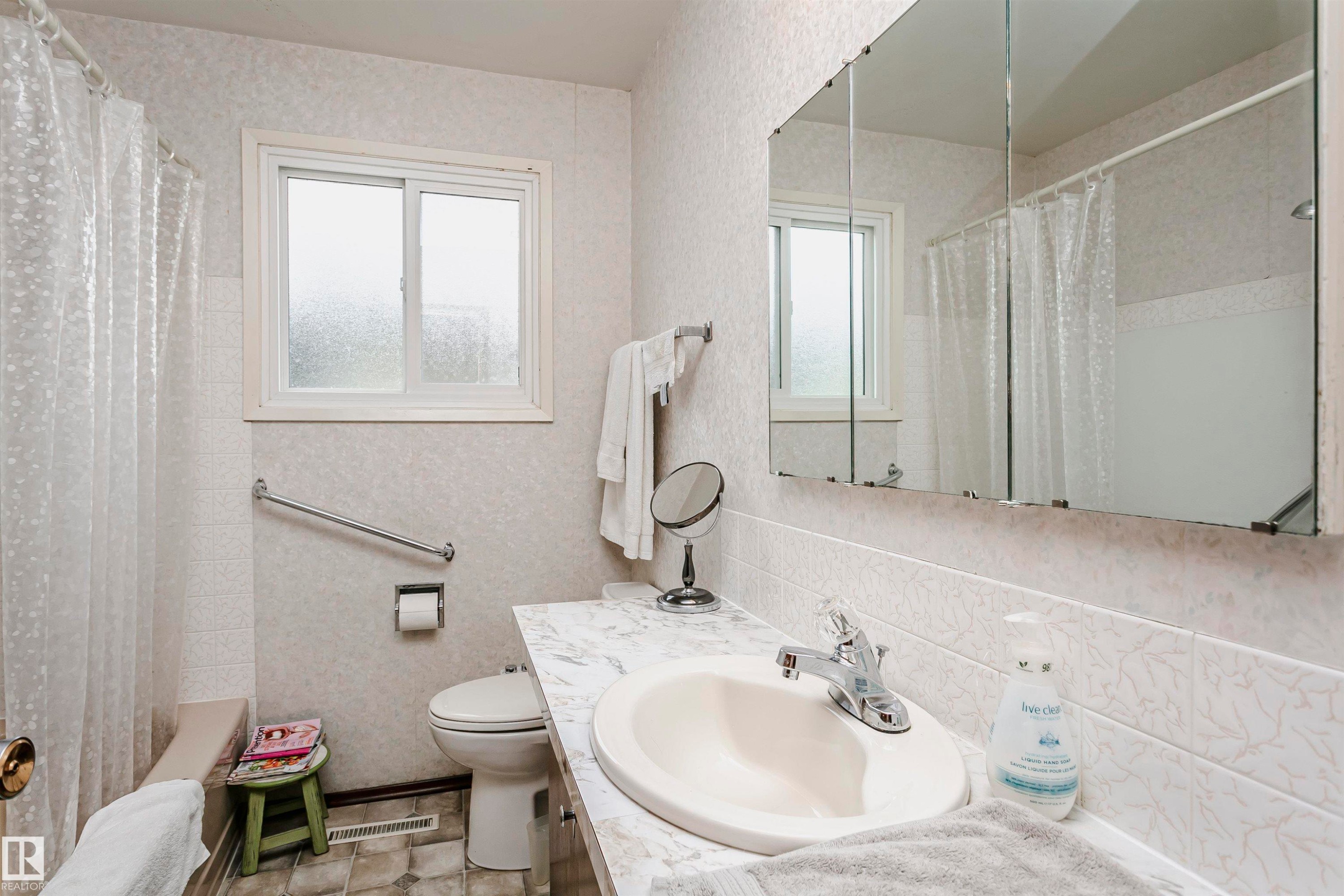 Bathroom featuring a single-pane window with frosted glass, a white toilet, and a white integrated sink set into a laminate countertop - 14231 80 Street, Edmonton, AB