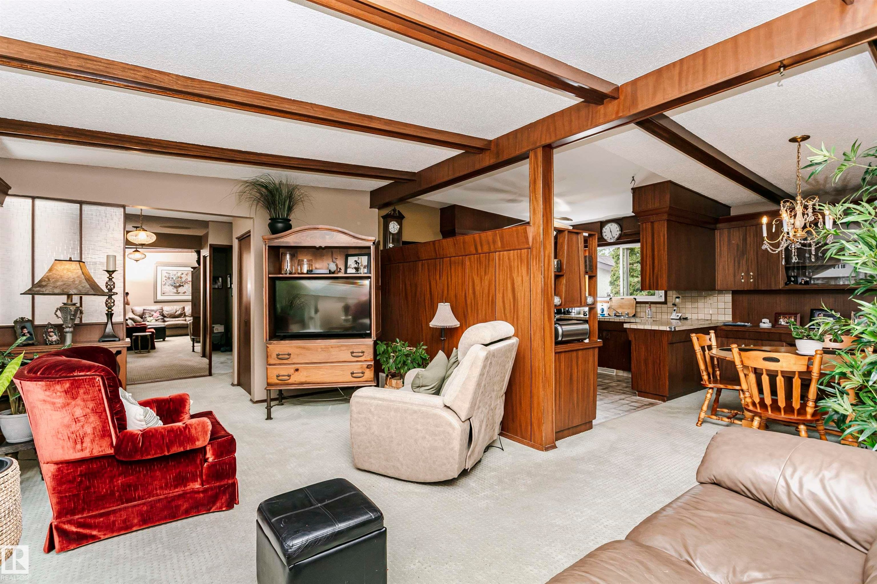 Open-concept living space featuring exposed wood ceiling beams, wood-paneled accents, and light-colored carpeting - 14231 80 Street, Edmonton, AB