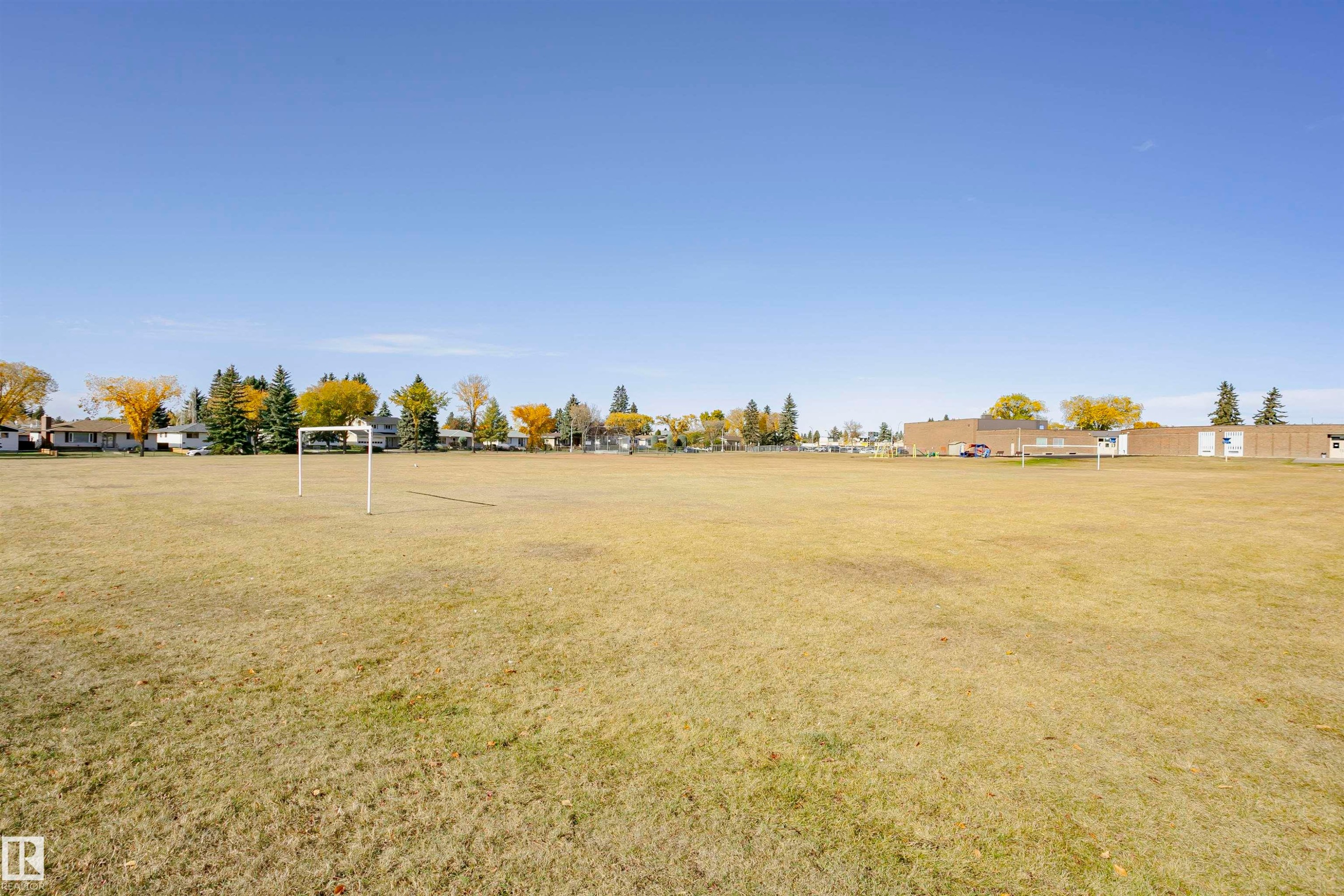 Expansive open field with two goalposts, bordered by mature trees and residential properties - 14231 80 Street, Edmonton, AB