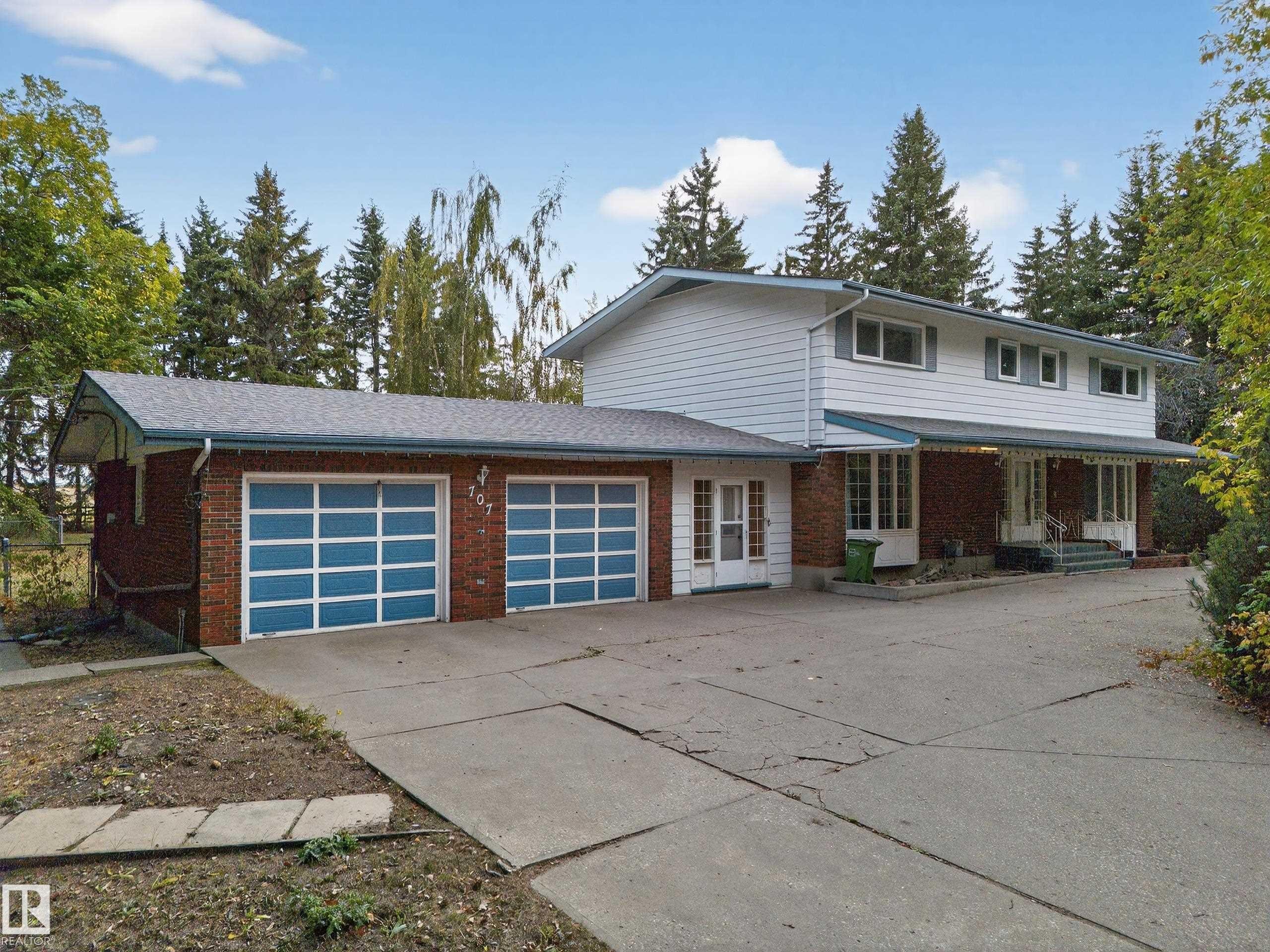 Two-story residence featuring a brick and siding exterior, an attached two-car garage with contemporary glass panel doors, a covered front porch, and mature surrounding trees - 707 65 Avenue, Edmonton, AB