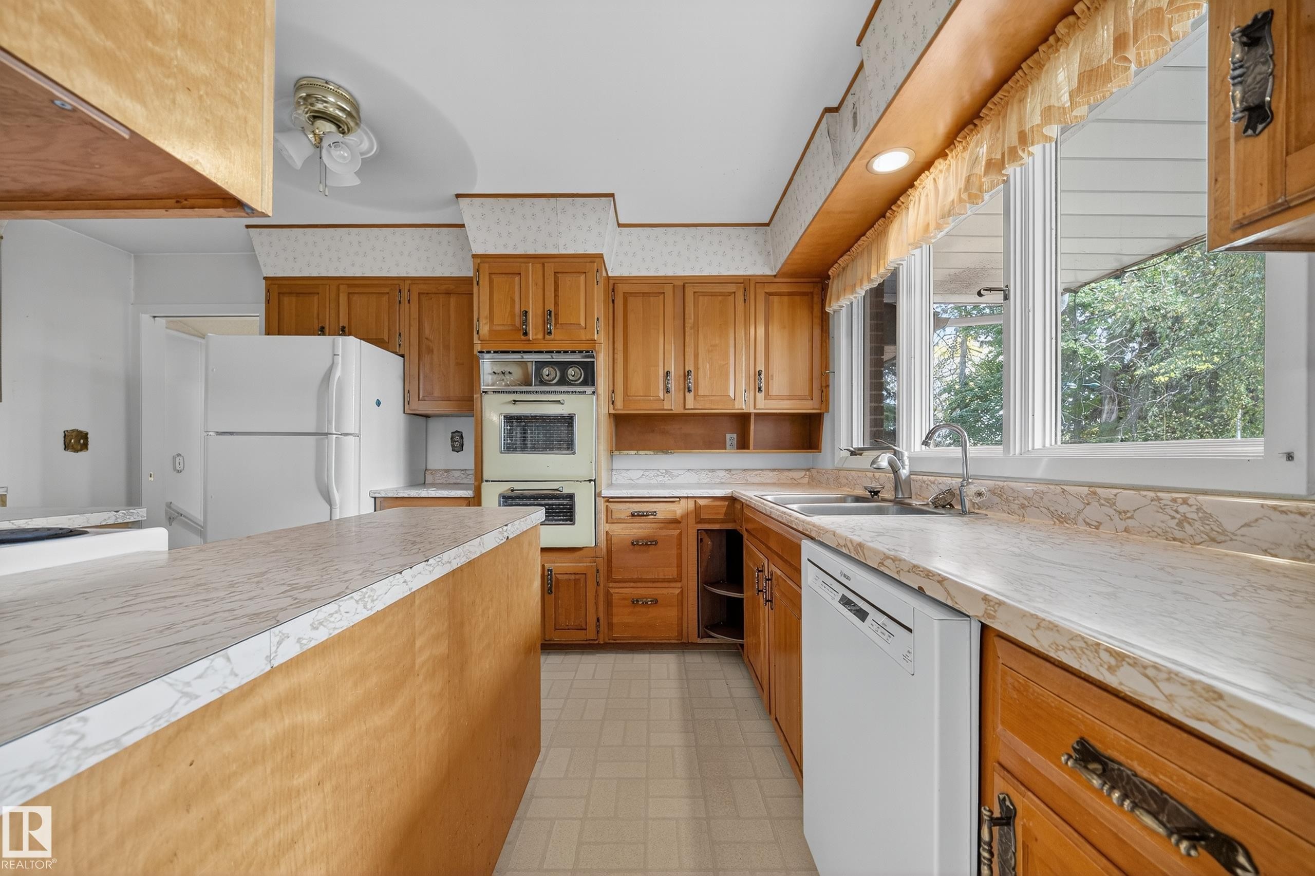Kitchen featuring wood cabinetry, laminate countertops, a built-in double oven, and a window overlooking exterior foliage - 707 65 Avenue, Edmonton, AB