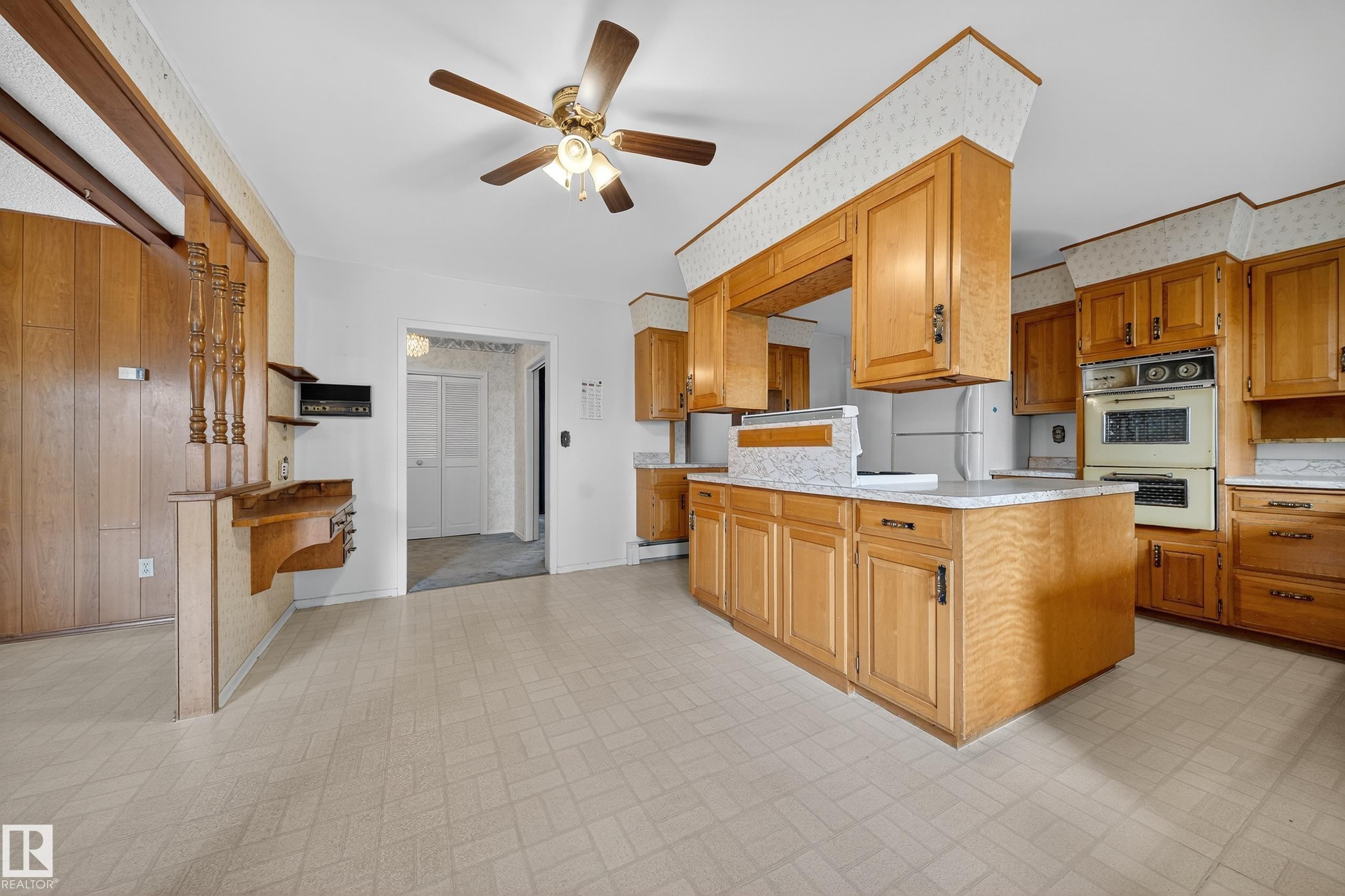Kitchen featuring extensive wood cabinetry with dark hardware, a built-in double oven, and a central island with a light-colored countertop - 707 65 Avenue, Edmonton, AB