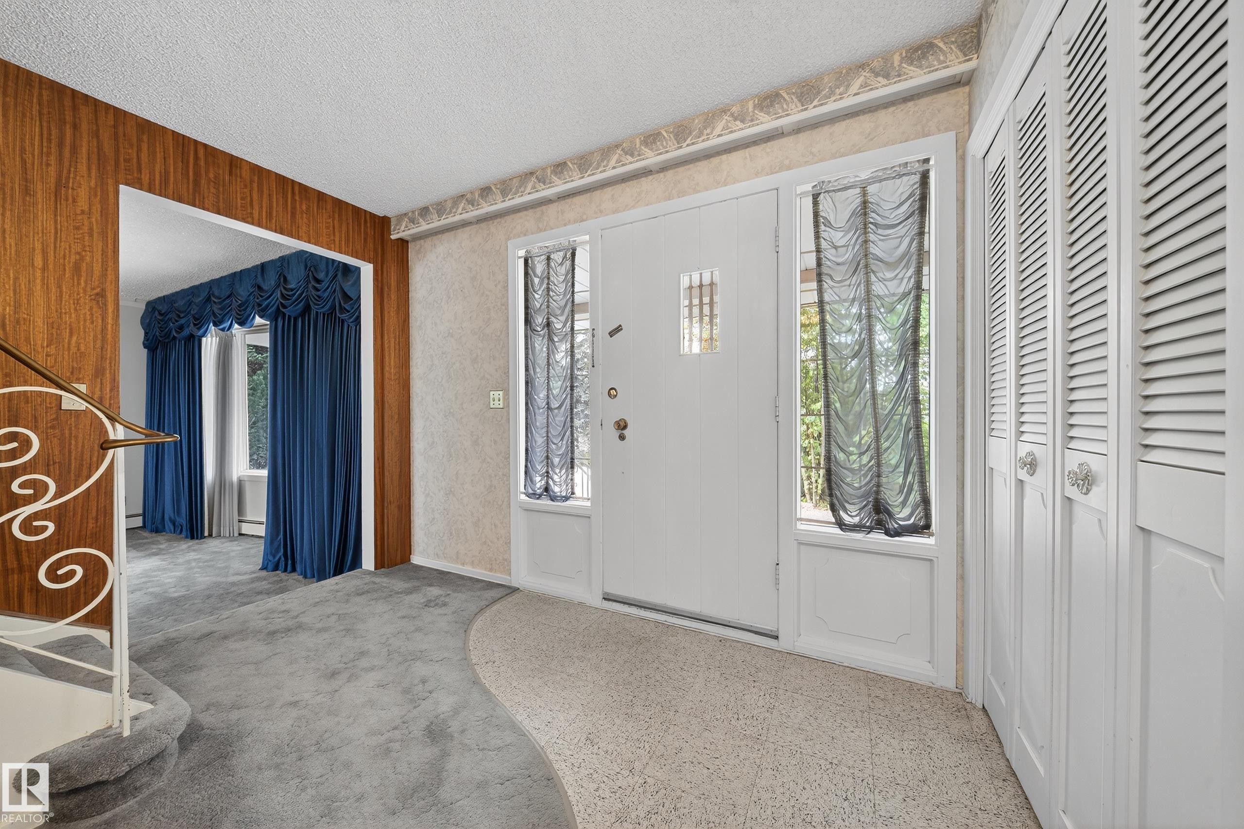 Entryway featuring a solid white door with side lights, louvered bi-fold closet doors, and wood-panel accent wall - 707 65 Avenue, Edmonton, AB