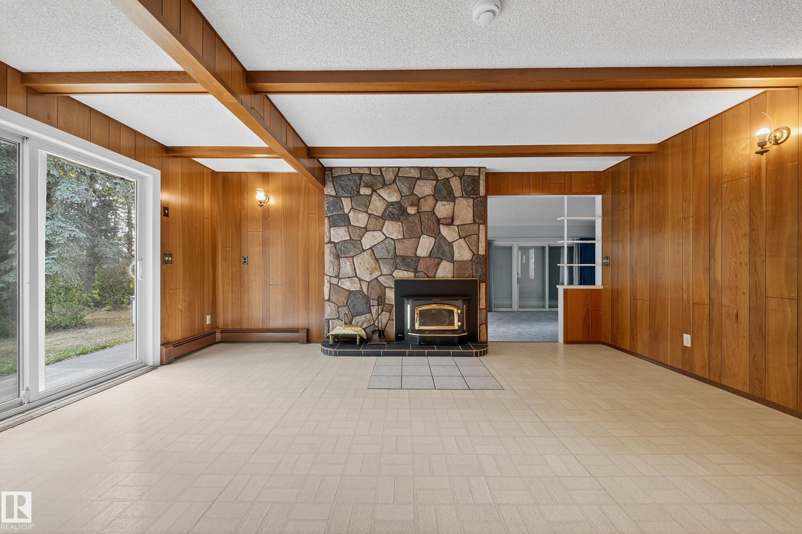 Expansive room featuring a prominent stone fireplace with an insert and hearth, wood-paneled walls, exposed wood beams, and patterned tile flooring - 707 65 Avenue, Edmonton, AB