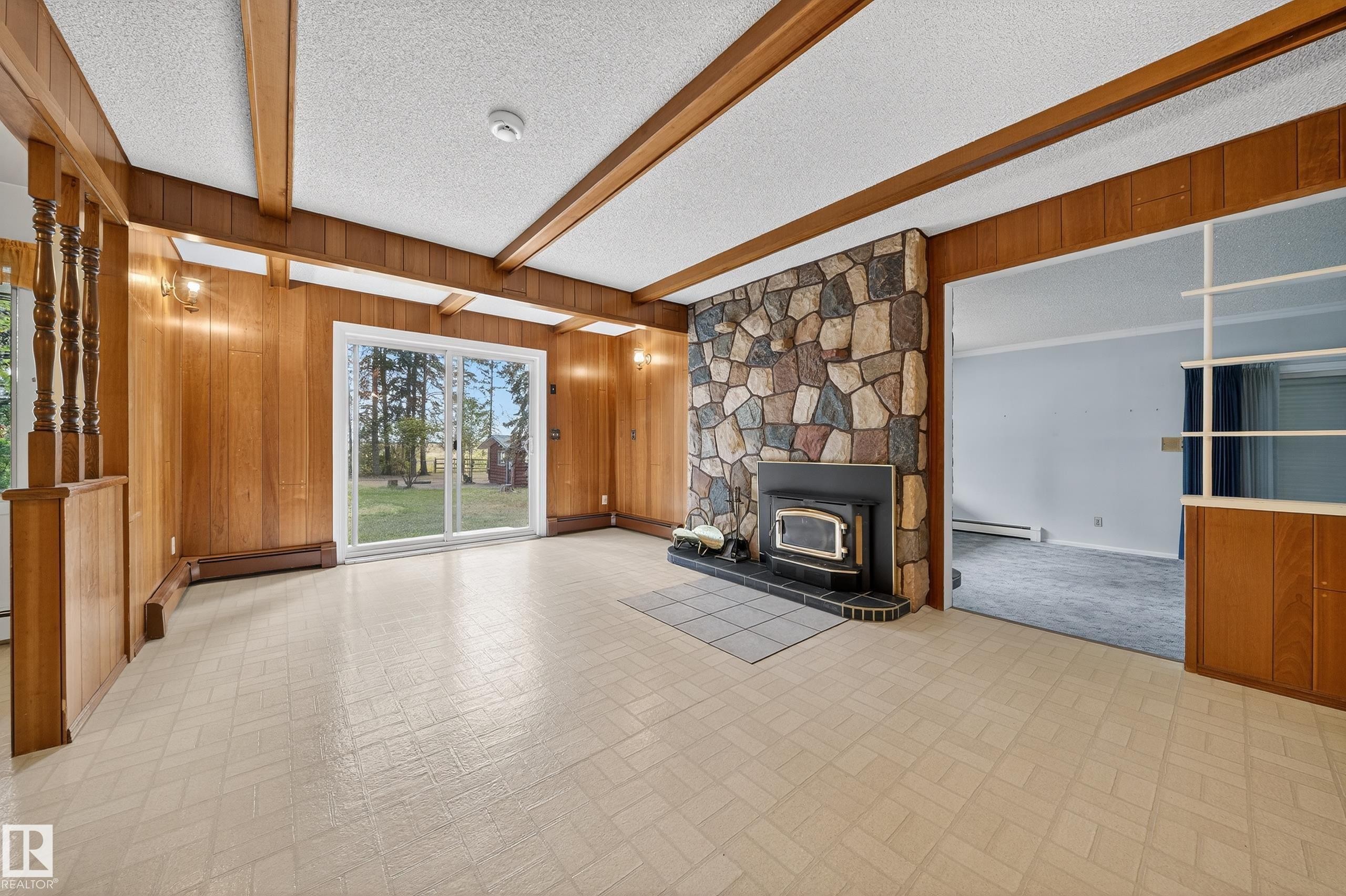 Spacious living area featuring a stone fireplace with a wood-burning insert, wood paneling, exposed ceiling beams, and sliding glass doors to the exterior - 707 65 Avenue, Edmonton, AB