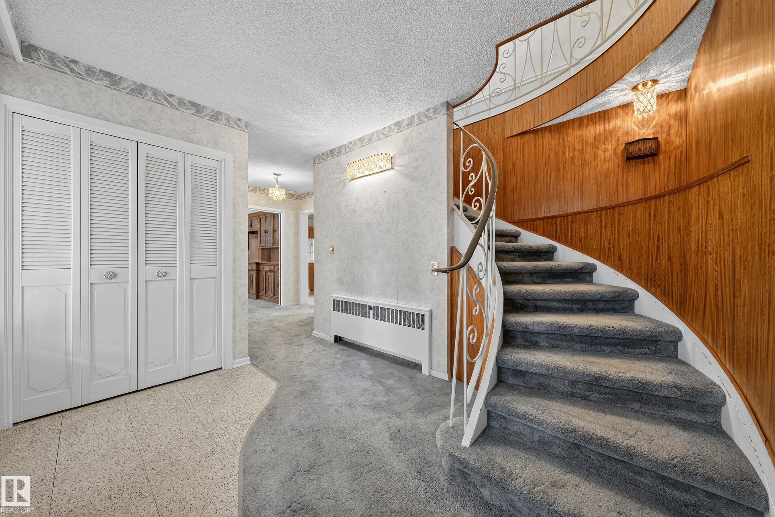 Curved staircase with decorative wrought iron railing, wood-paneled wall, textured wallpaper, carpeted flooring, and built-in bifold doors - 707 65 Avenue, Edmonton, AB
