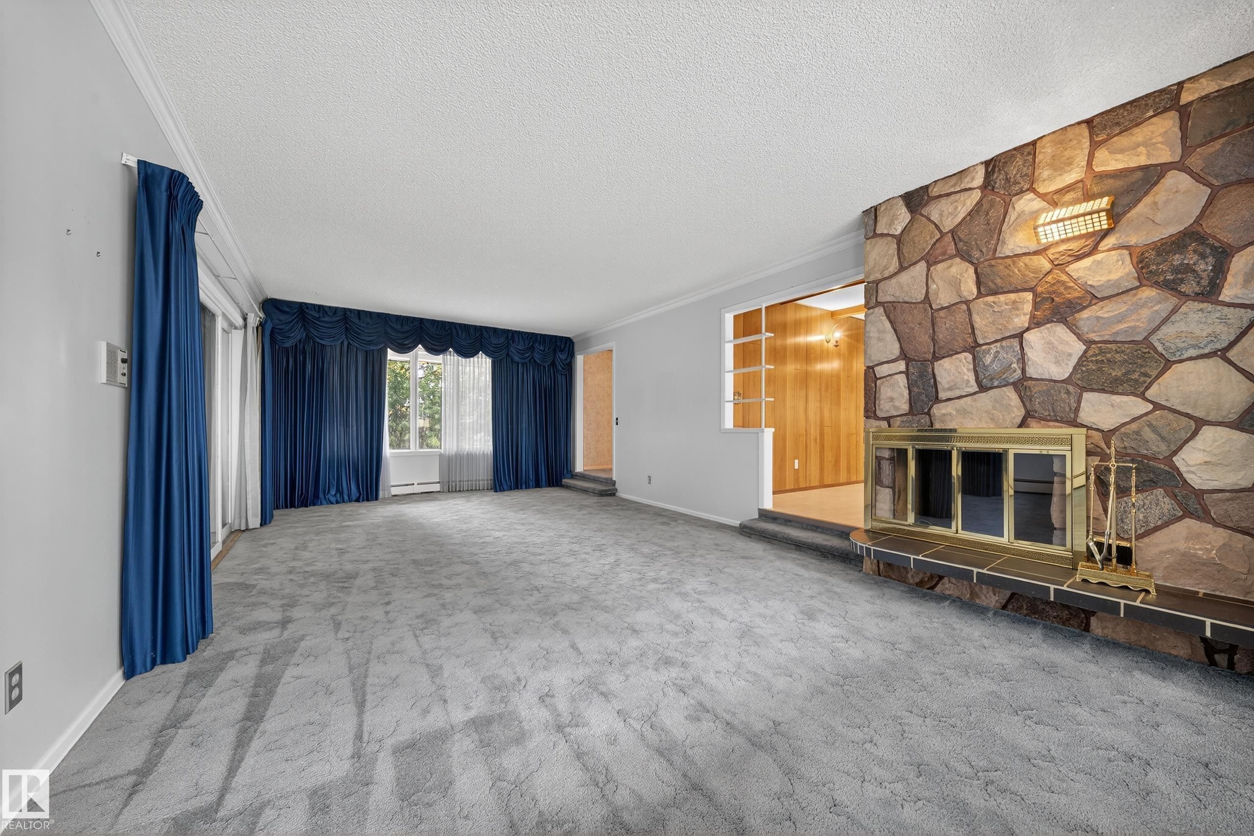 Living area featuring a stone accent wall with a fireplace, brass firebox, and a stone hearth - 707 65 Avenue, Edmonton, AB