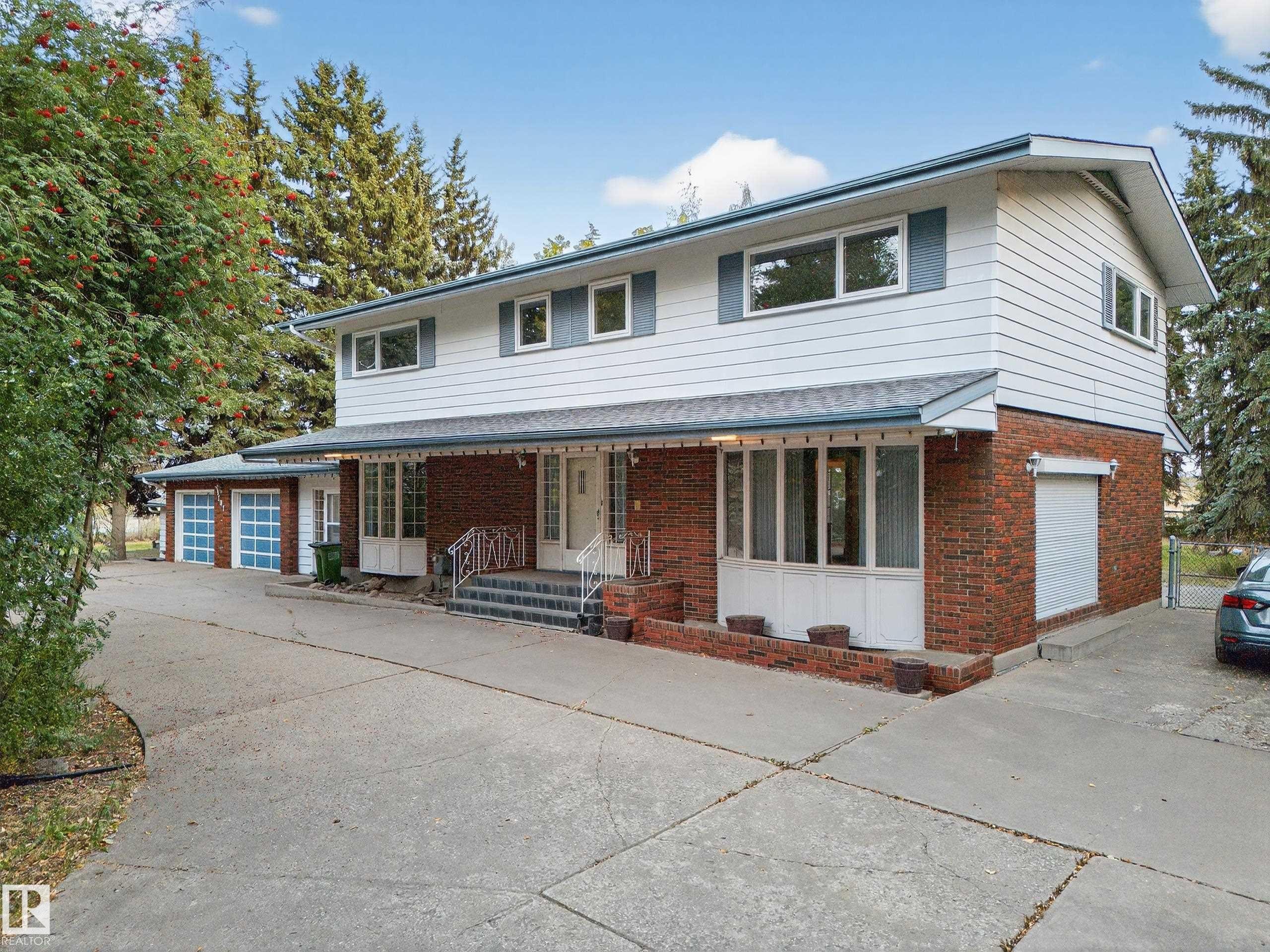 Two-story residence featuring brick and siding exterior, multiple garage doors, and a covered front entry - 707 65 Avenue, Edmonton, AB