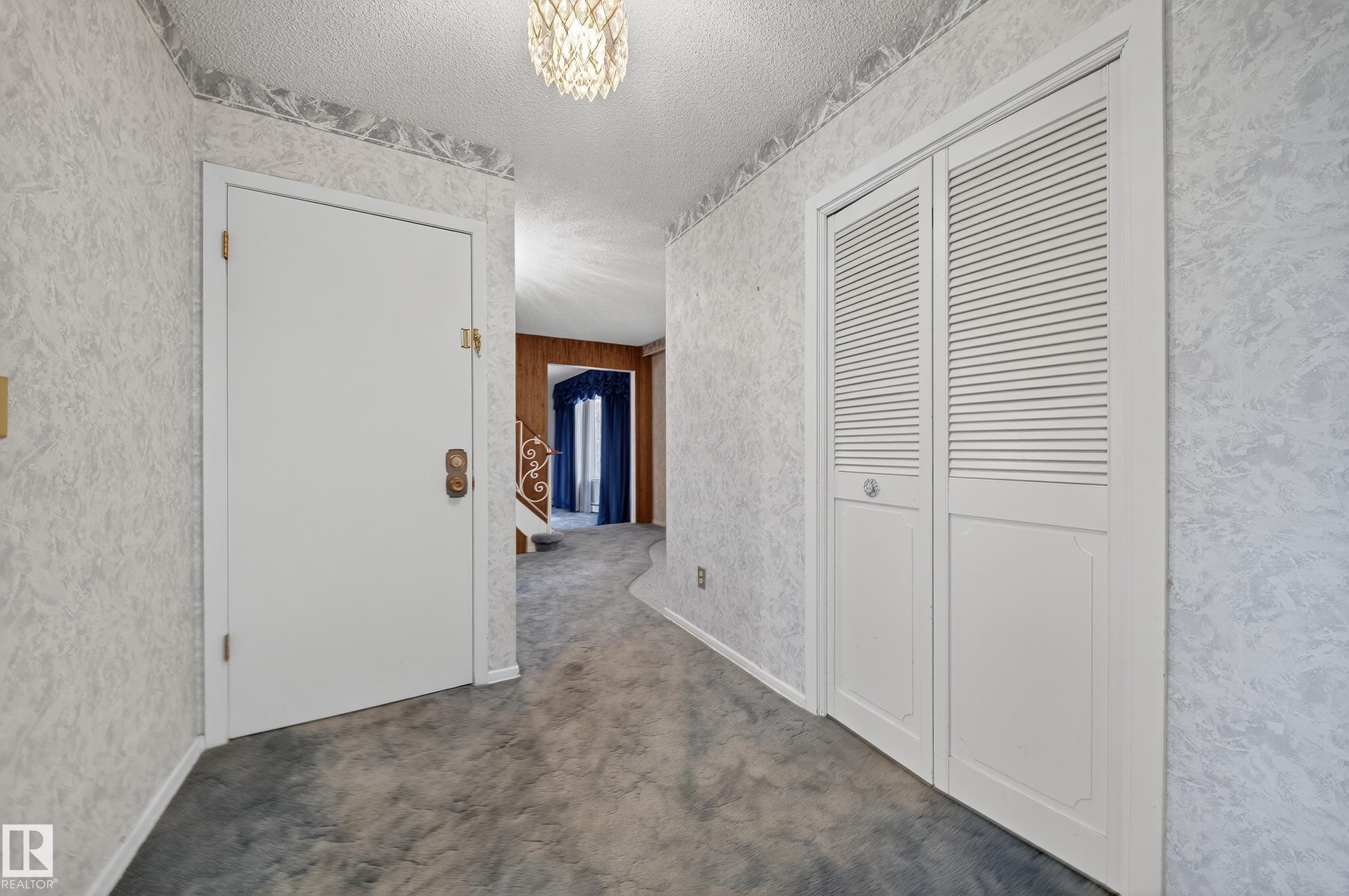 Entryway featuring textured wallpaper, plush carpeting, and a decorative ceiling light fixture - 707 65 Avenue, Edmonton, AB