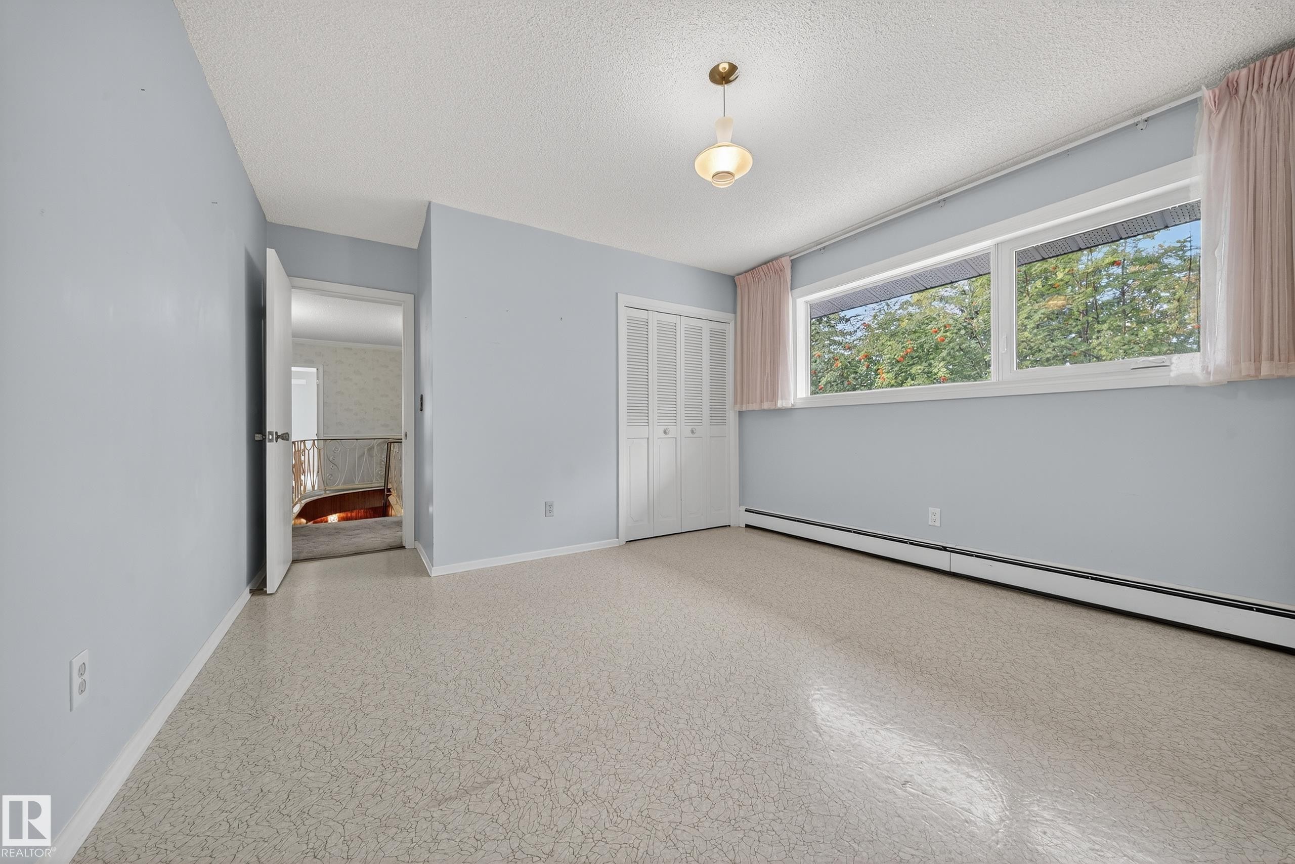 Spacious room featuring light-colored flooring, multiple windows, a ceiling-mounted light fixture, and bifold closet doors - 707 65 Avenue, Edmonton, AB