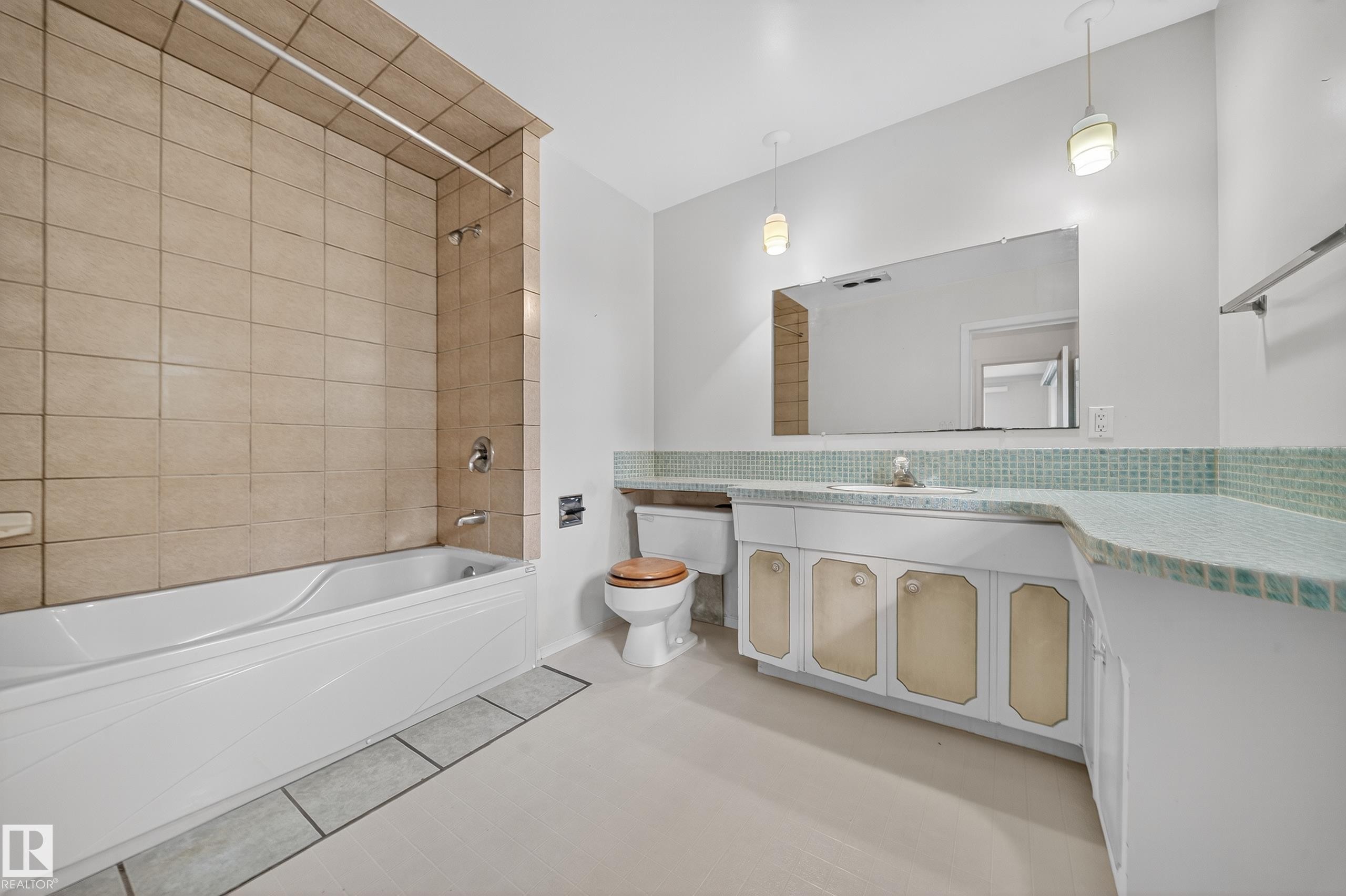 Bathroom featuring a white tub with light-toned tiled surround, an extended vanity with a built-in sink, and a mirrored wall - 707 65 Avenue, Edmonton, AB