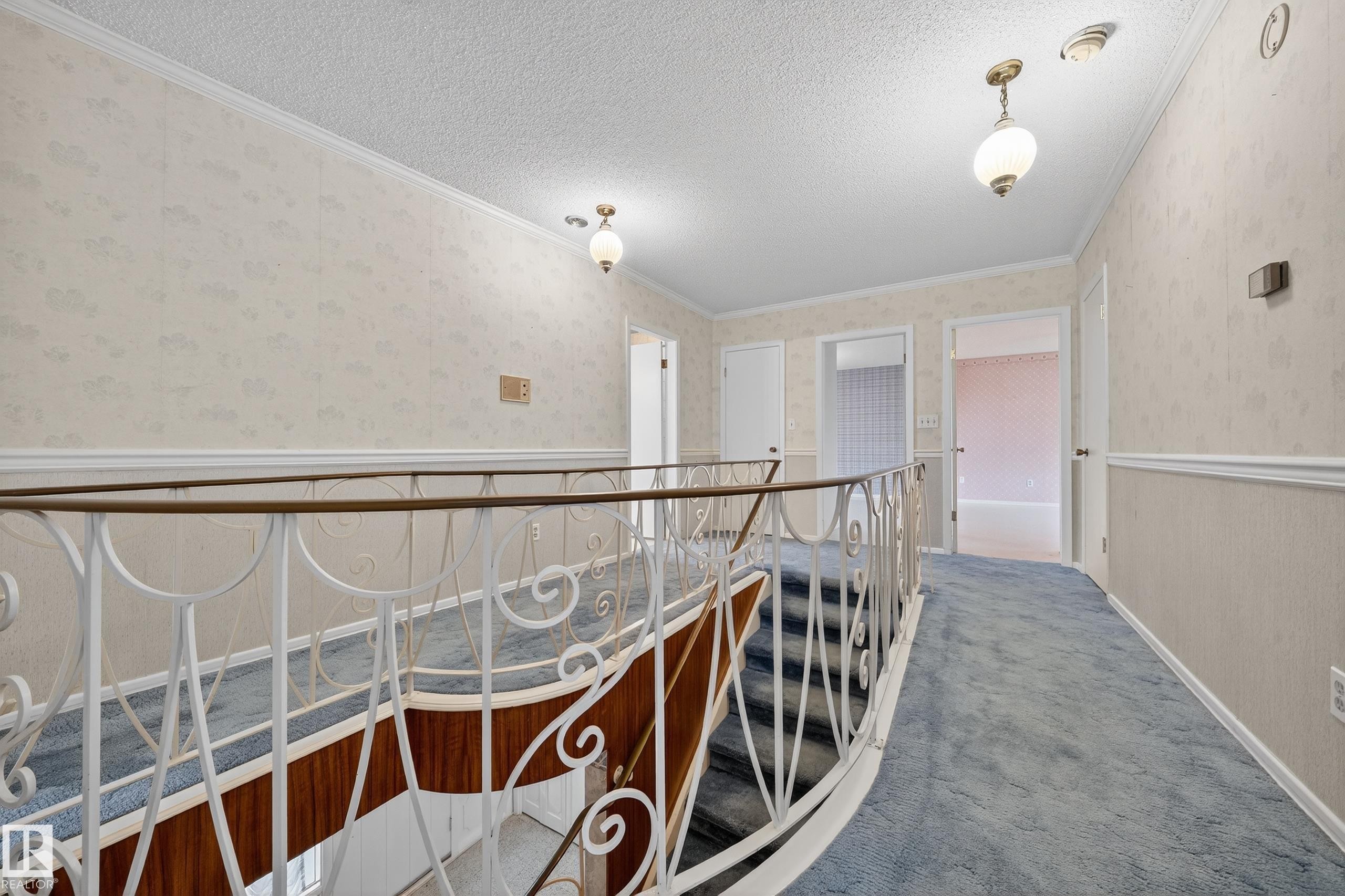 Upper level hallway featuring blue carpeting, decorative iron railing, and suspended light fixtures - 707 65 Avenue, Edmonton, AB