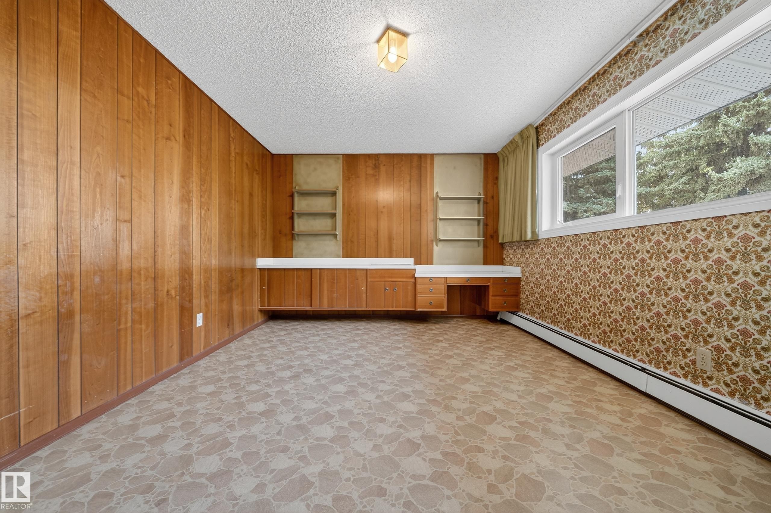 Room featuring wood paneling, a built-in desk with cabinetry, and a large window - 707 65 Avenue, Edmonton, AB