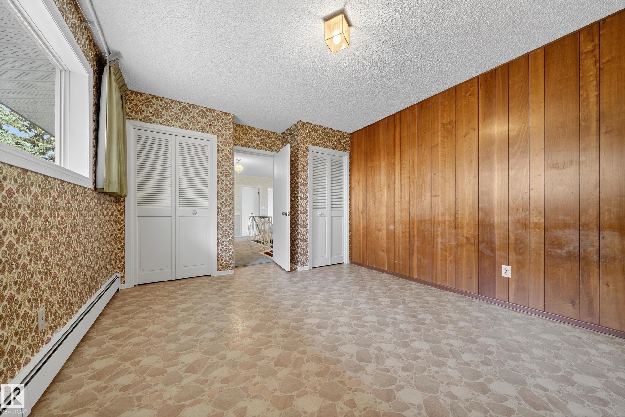 Room featuring a wood-panel accent wall and two white bi-fold closet doors - 707 65 Avenue, Edmonton, AB