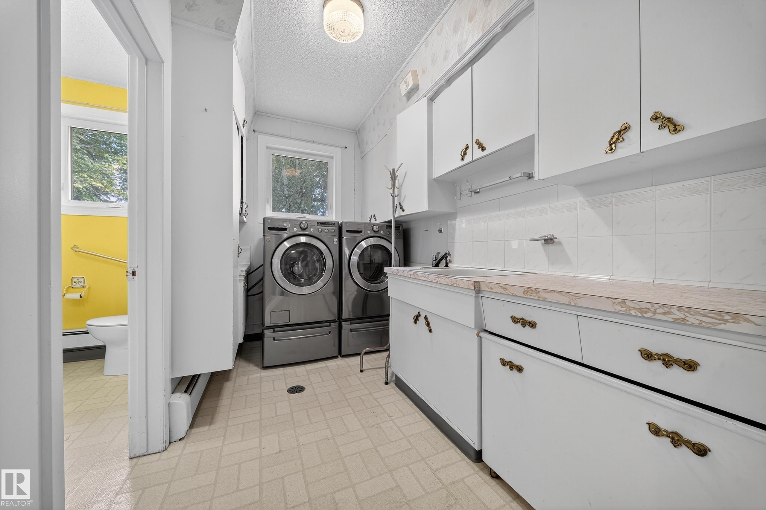 Laundry area featuring light-toned flooring, white cabinetry with ornate hardware, and a window for natural light - 707 65 Avenue, Edmonton, AB