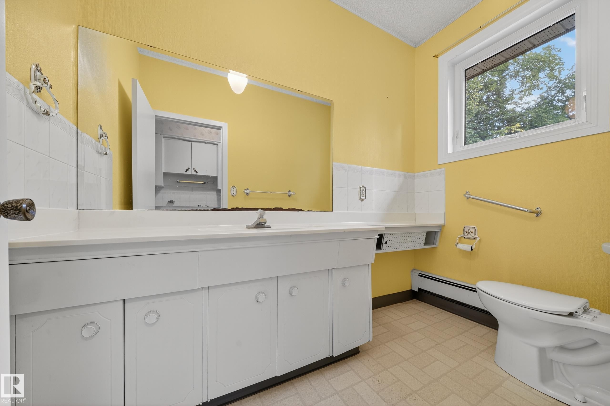 Expansive vanity with integrated sink, a large wall-mounted mirror, and white cabinetry - 707 65 Avenue, Edmonton, AB