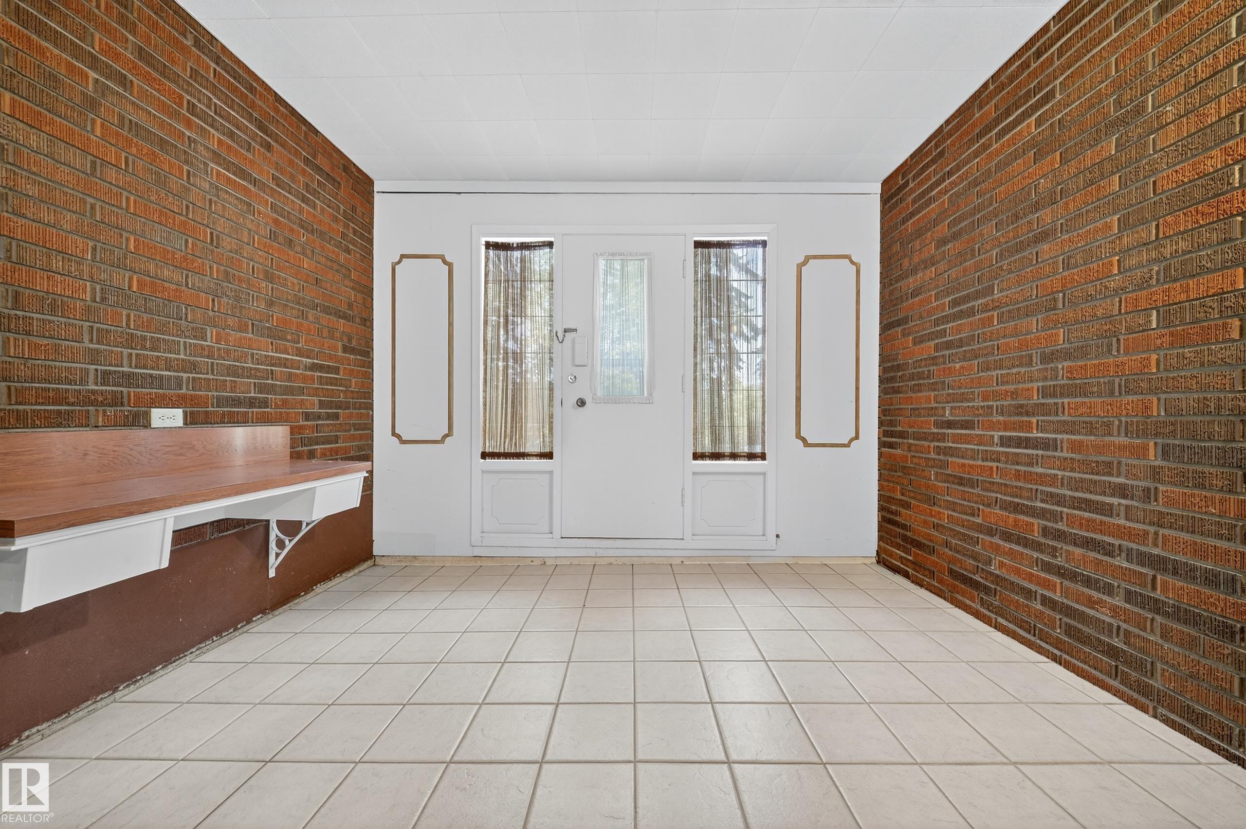 Entryway featuring brick accent walls, light-toned square tile flooring, and a white double door with upper glass panels - 707 65 Avenue, Edmonton, AB