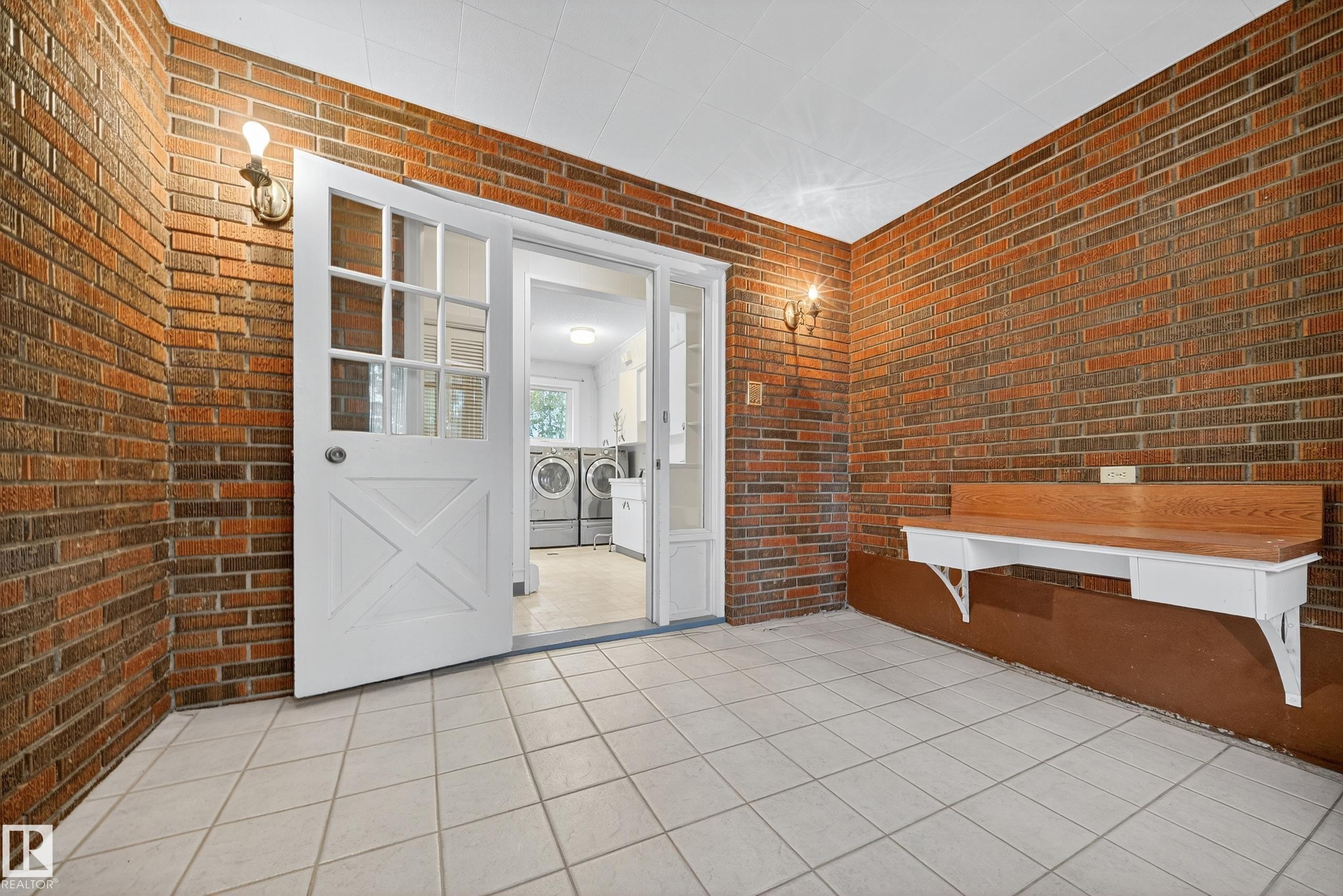 Brick-walled interior space featuring a white tile floor and a built-in wood-top bench - 707 65 Avenue, Edmonton, AB