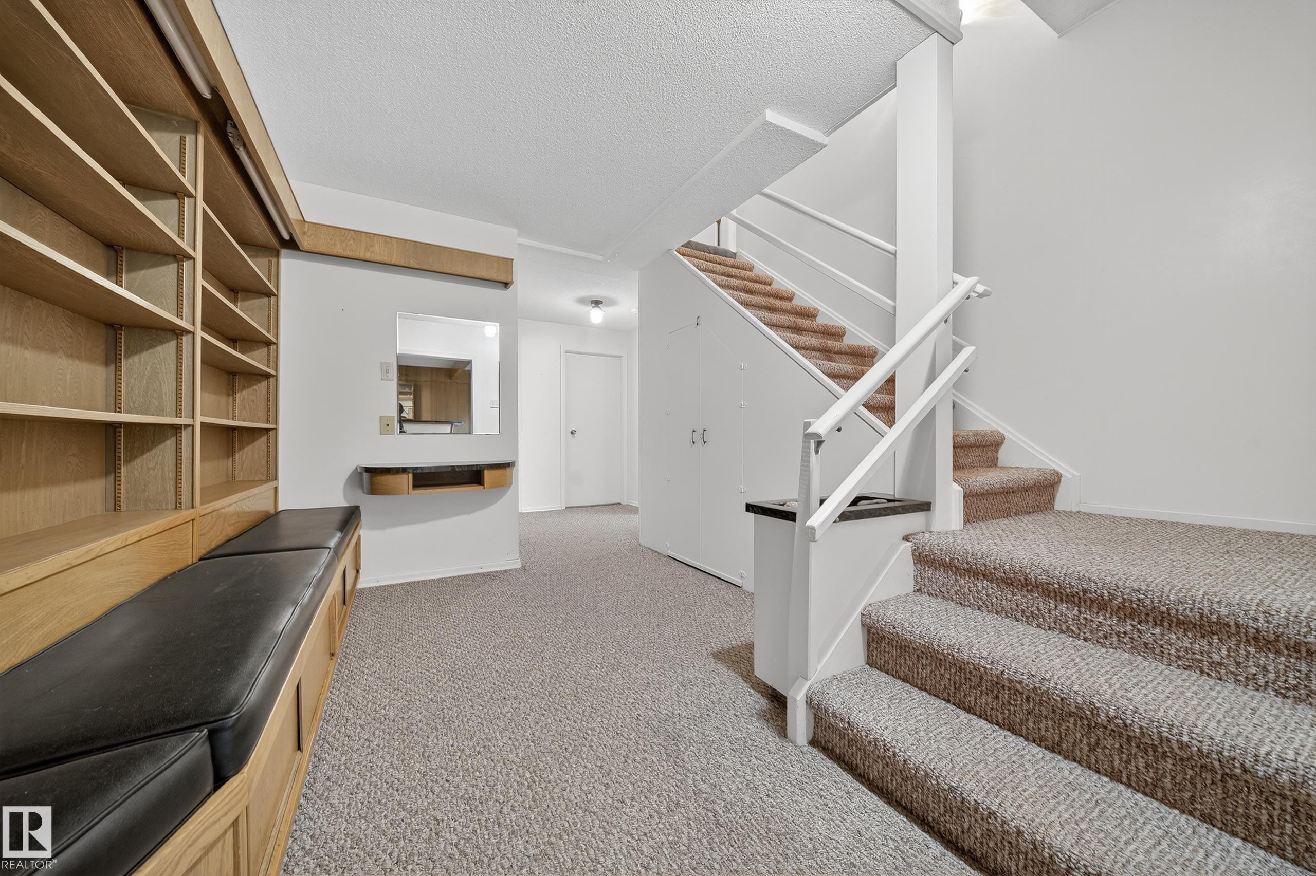Built-in wood-finish shelving with integrated bench seating, carpeted staircase with white railings, and a wall-mounted mirror with a wood-finish shelf - 707 65 Avenue, Edmonton, AB