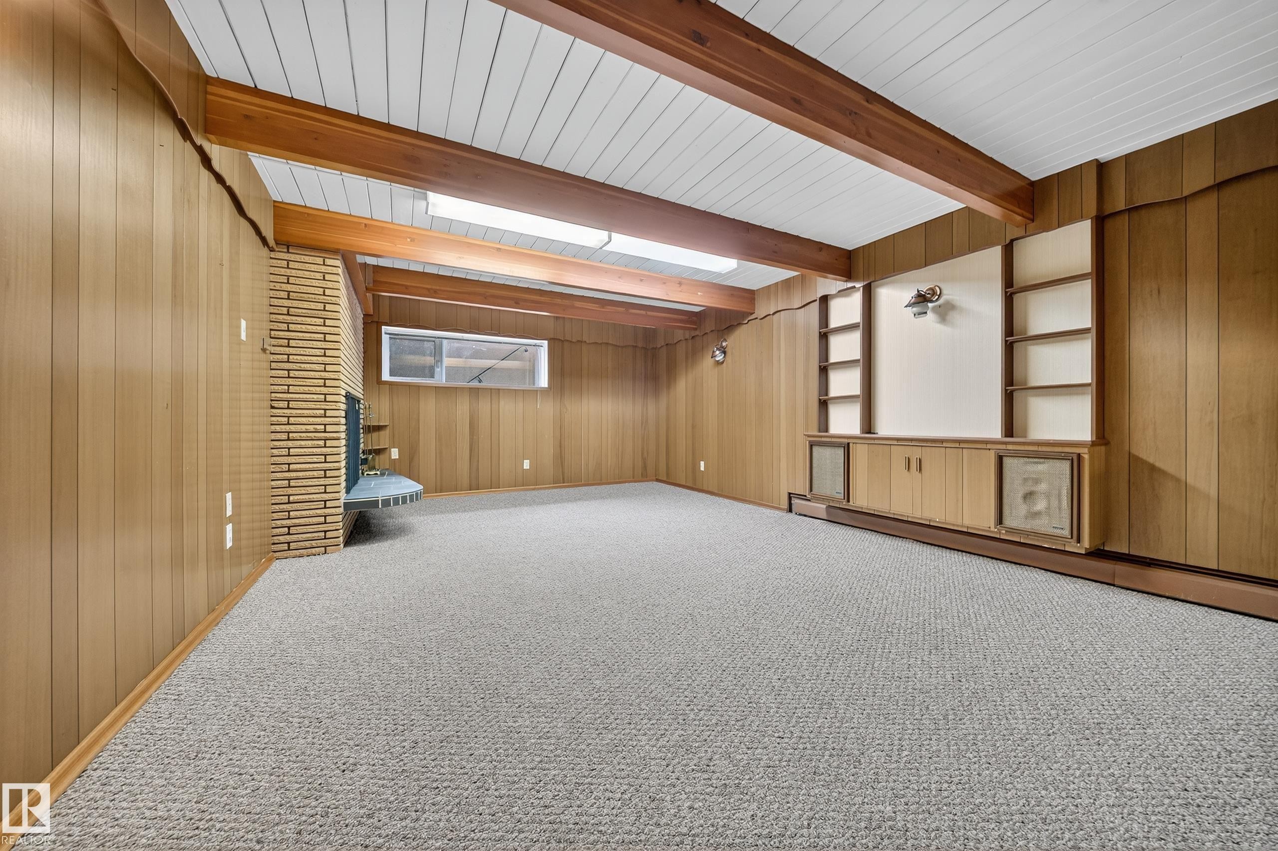 Spacious room featuring wood-paneled walls, exposed wood beams, and textured carpet flooring - 707 65 Avenue, Edmonton, AB