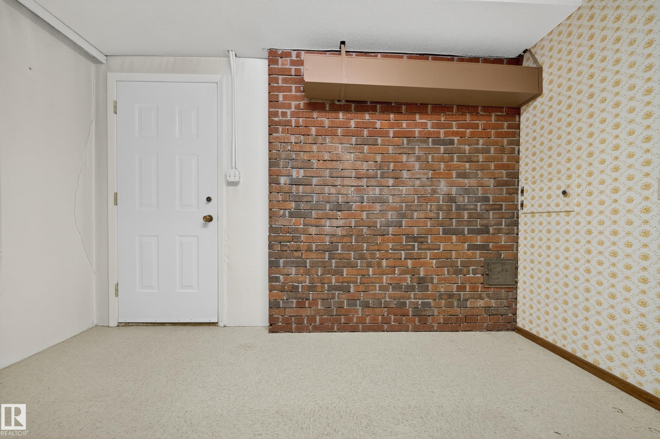Interior space featuring a white paneled door, exposed brick wall, patterned wallpaper, wall-to-wall carpeting, and baseboard trim - 707 65 Avenue, Edmonton, AB