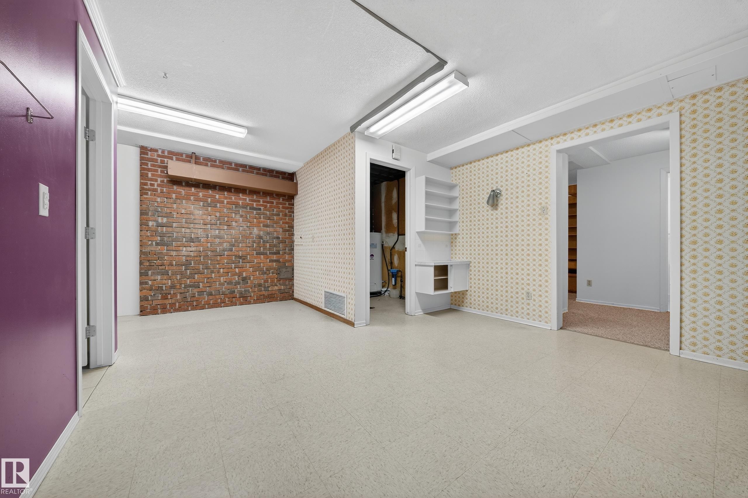 Spacious room with light-colored flooring, exposed brick accent wall, built-in shelving, and multiple doorways - 707 65 Avenue, Edmonton, AB