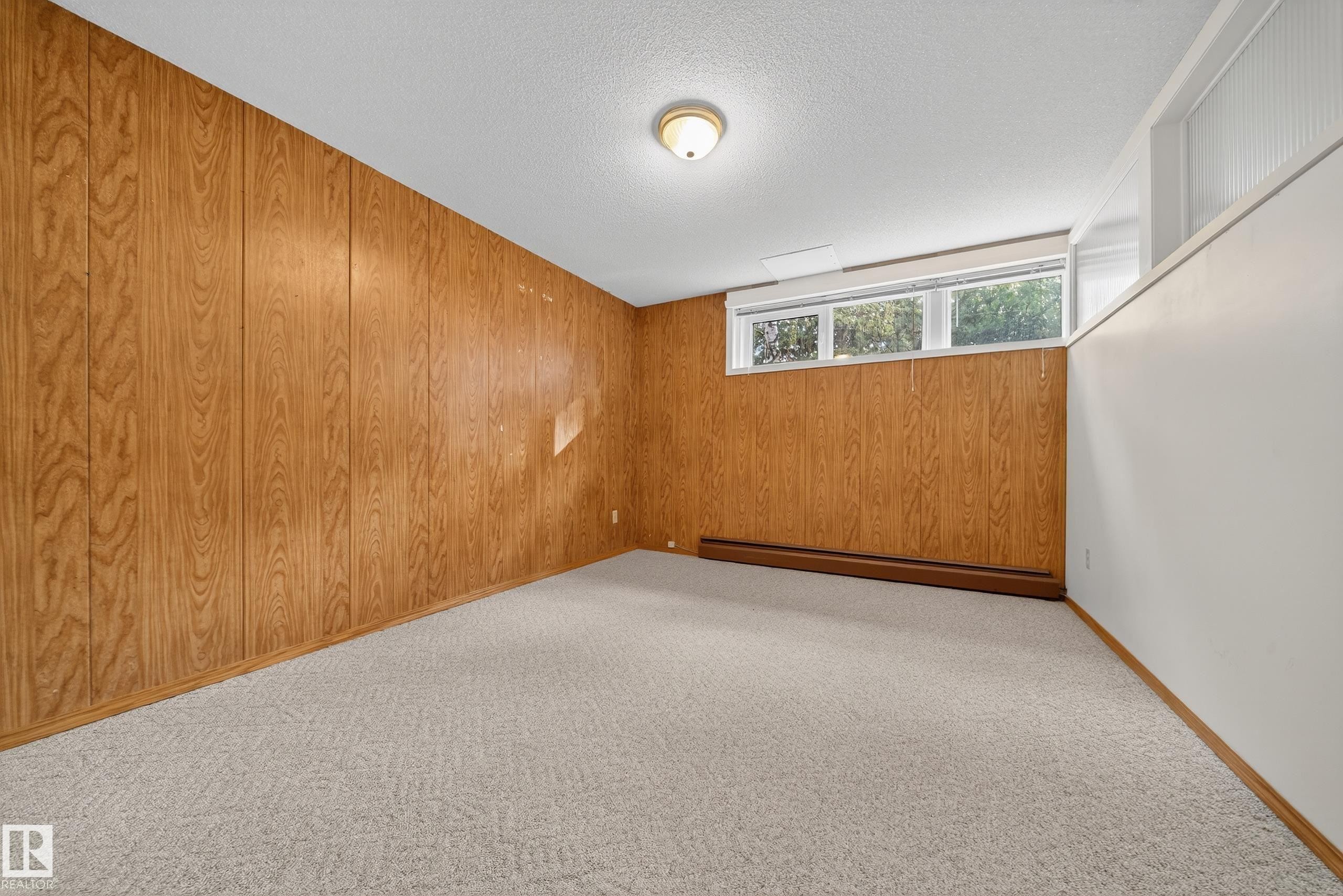 Spacious room featuring wood paneling on one wall, light-colored carpeting, three transom windows, a white painted wall, and a ceiling-mounted light fixture - 707 65 Avenue, Edmonton, AB