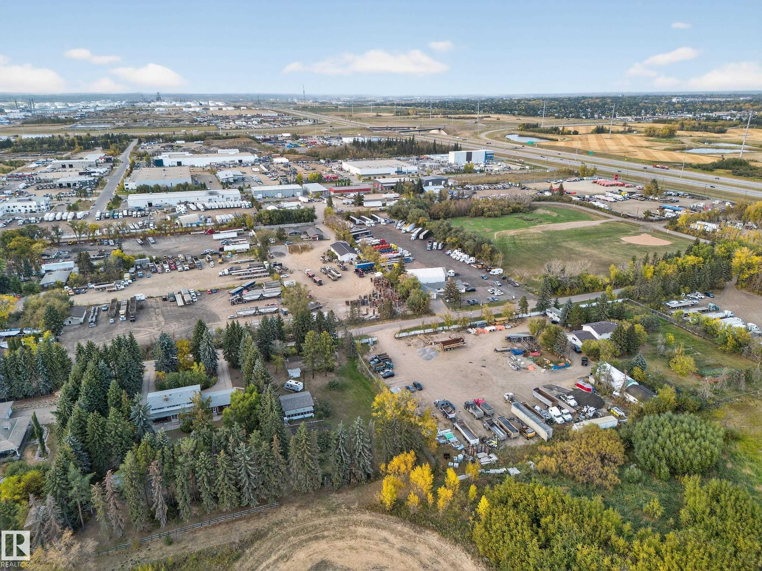 Aerial perspective showcasing an expansive industrial area with multiple commercial structures, open storage yards, and surrounding mature trees - 707 65 Avenue, Edmonton, AB