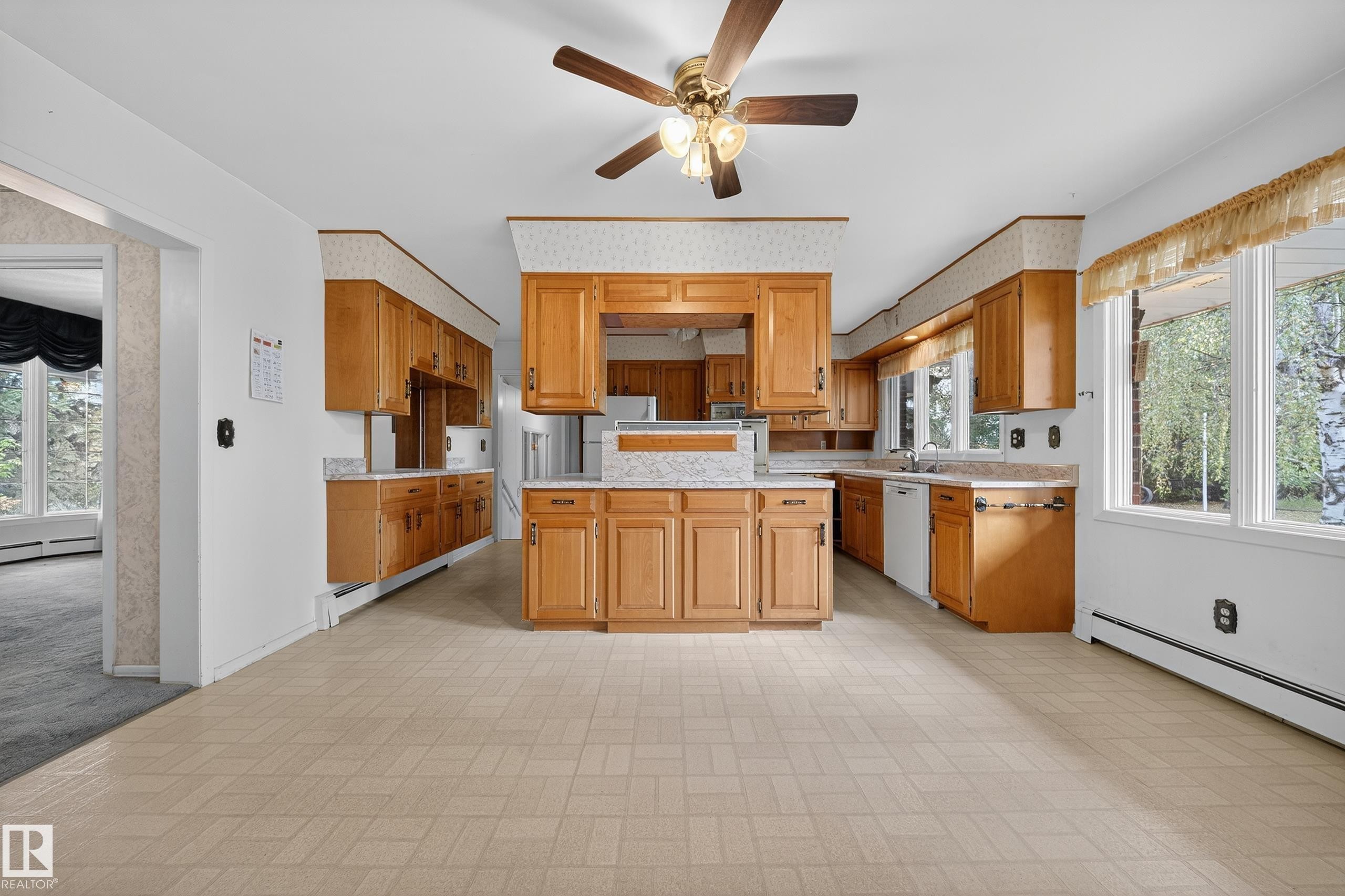 Spacious kitchen featuring extensive wood cabinetry, light-toned tiled flooring, and a central island with a multi-level countertop - 707 65 Avenue, Edmonton, AB