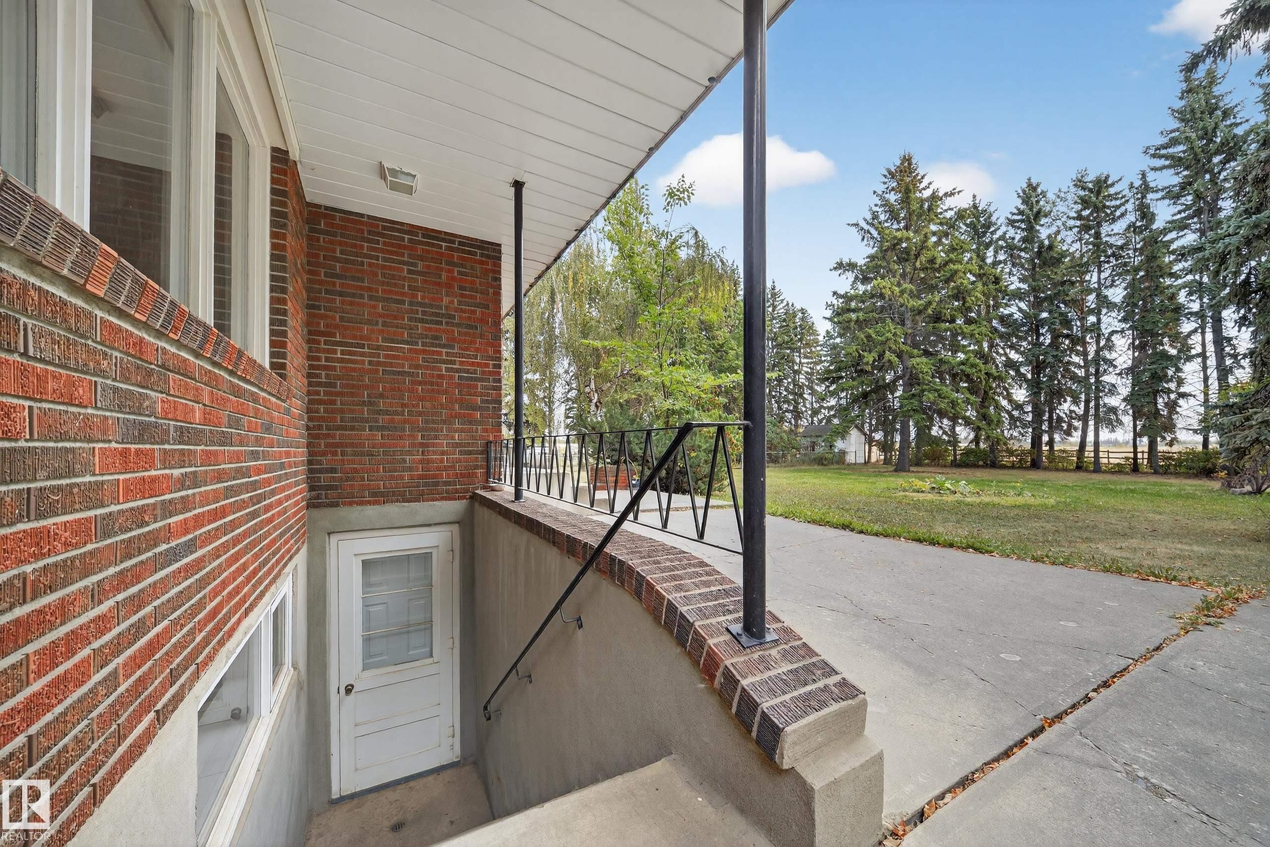 Brick exterior featuring a covered entryway with white soffit, black metal railing, and a ground-level access door - 707 65 Avenue, Edmonton, AB