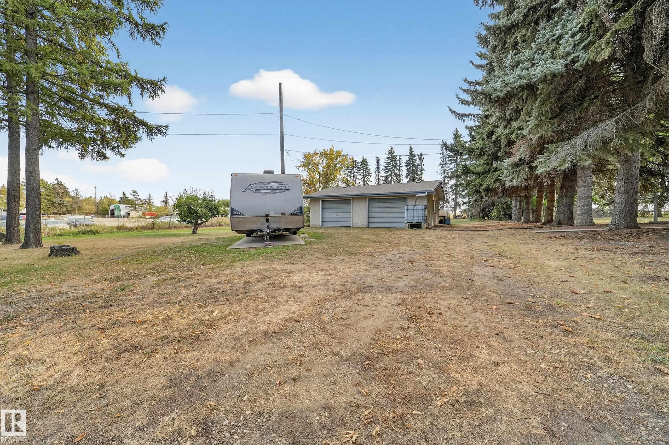 Detached two-car garage with roll-up doors, accompanied by mature evergreen trees - 707 65 Avenue, Edmonton, AB