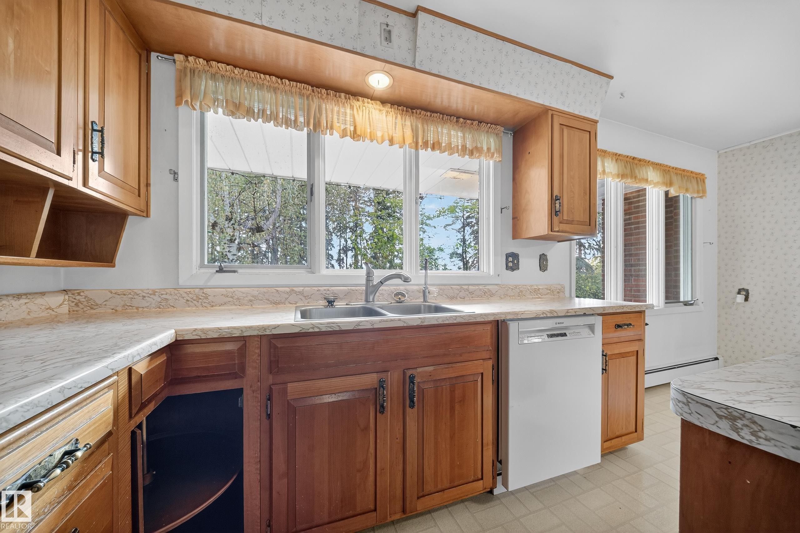 Kitchen featuring wood cabinetry, a dual-basin stainless steel sink with a gooseneck faucet, light-toned countertops, and a white dishwasher - 707 65 Avenue, Edmonton, AB
