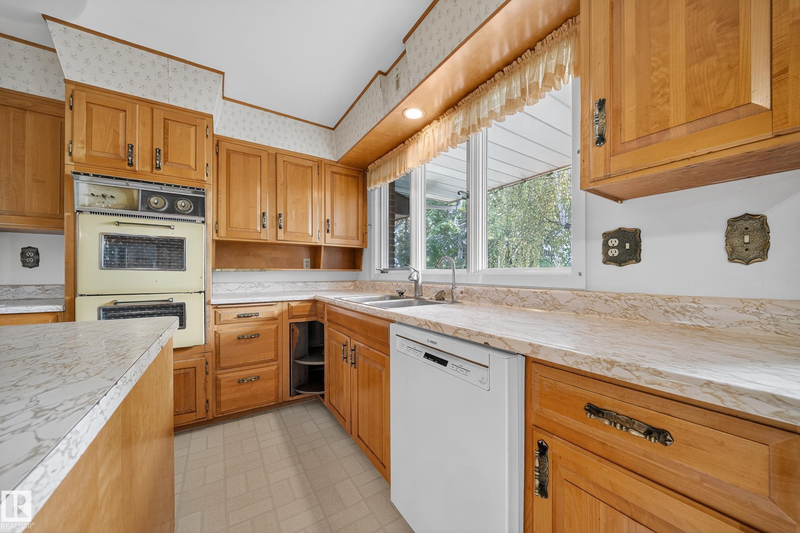Kitchen featuring wood cabinetry, light-colored countertops, a double wall oven, and a built-in dishwasher - 707 65 Avenue, Edmonton, AB