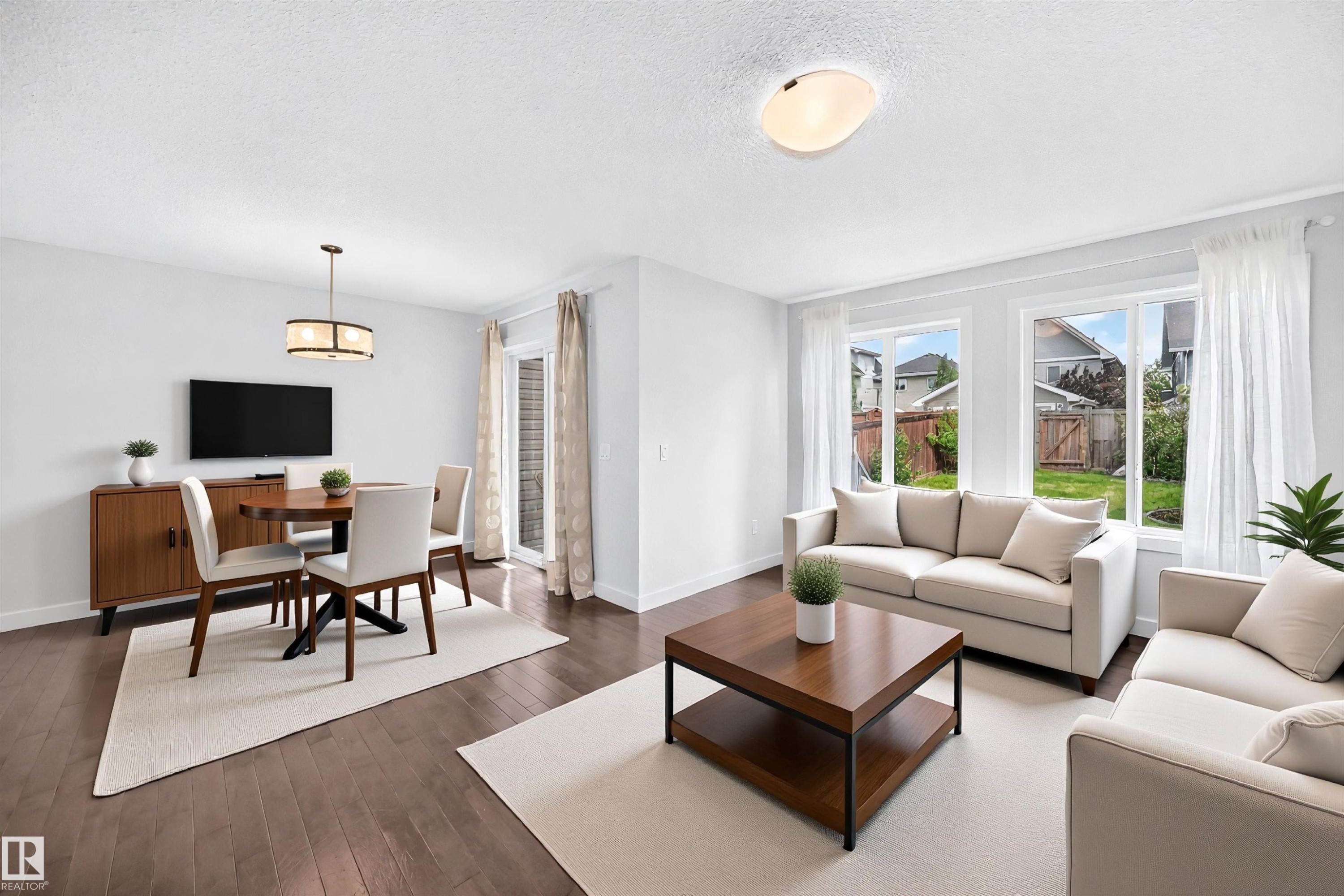 Open-concept living and dining areas featuring wood-finish flooring, abundant natural light from multiple windows, and a sliding glass door providing access to the backyard - 2433 Glenridding Boulevard, Edmonton, AB
